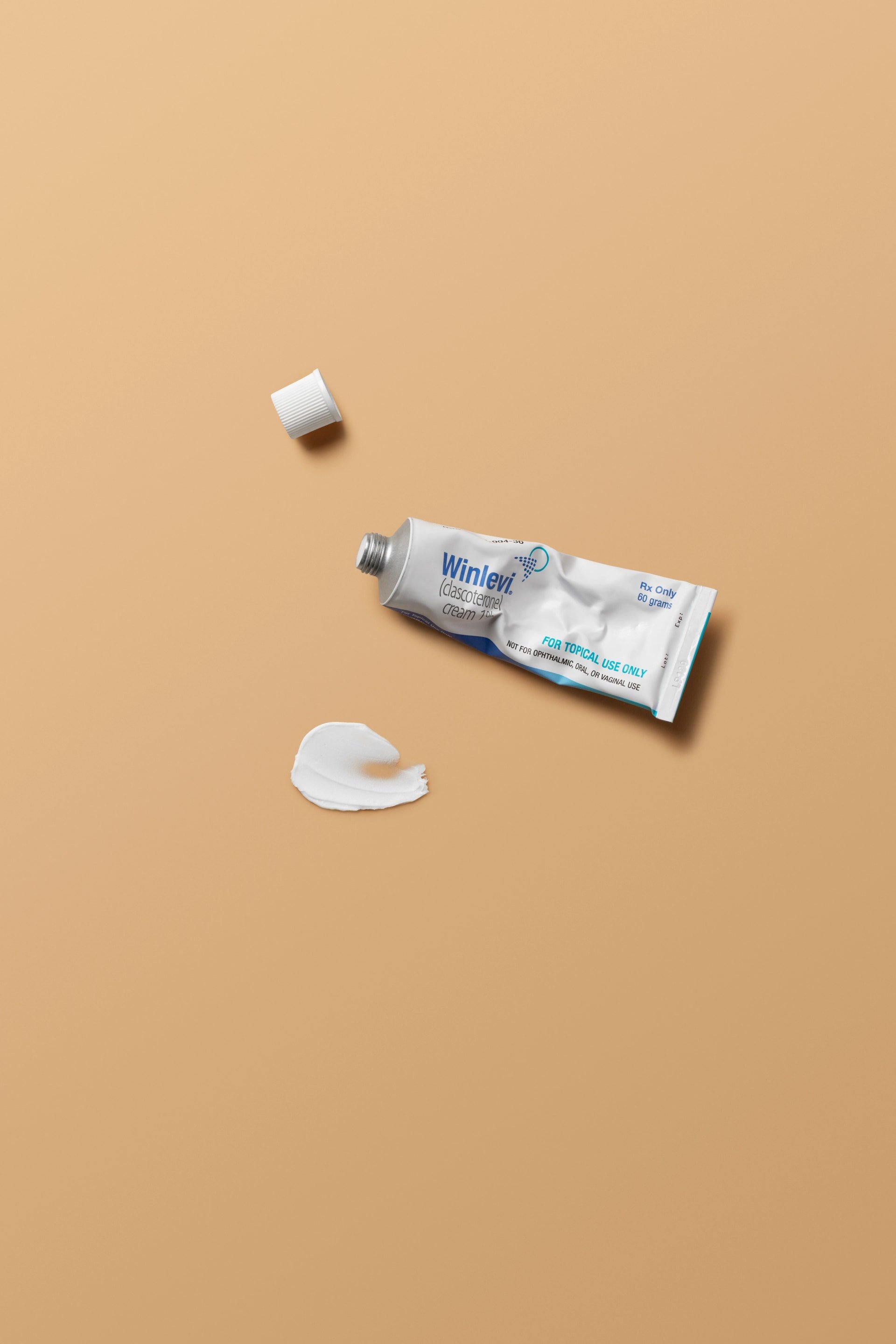 Tube of Winlevi topical cream on a beige background with a small amount of cream next to it.