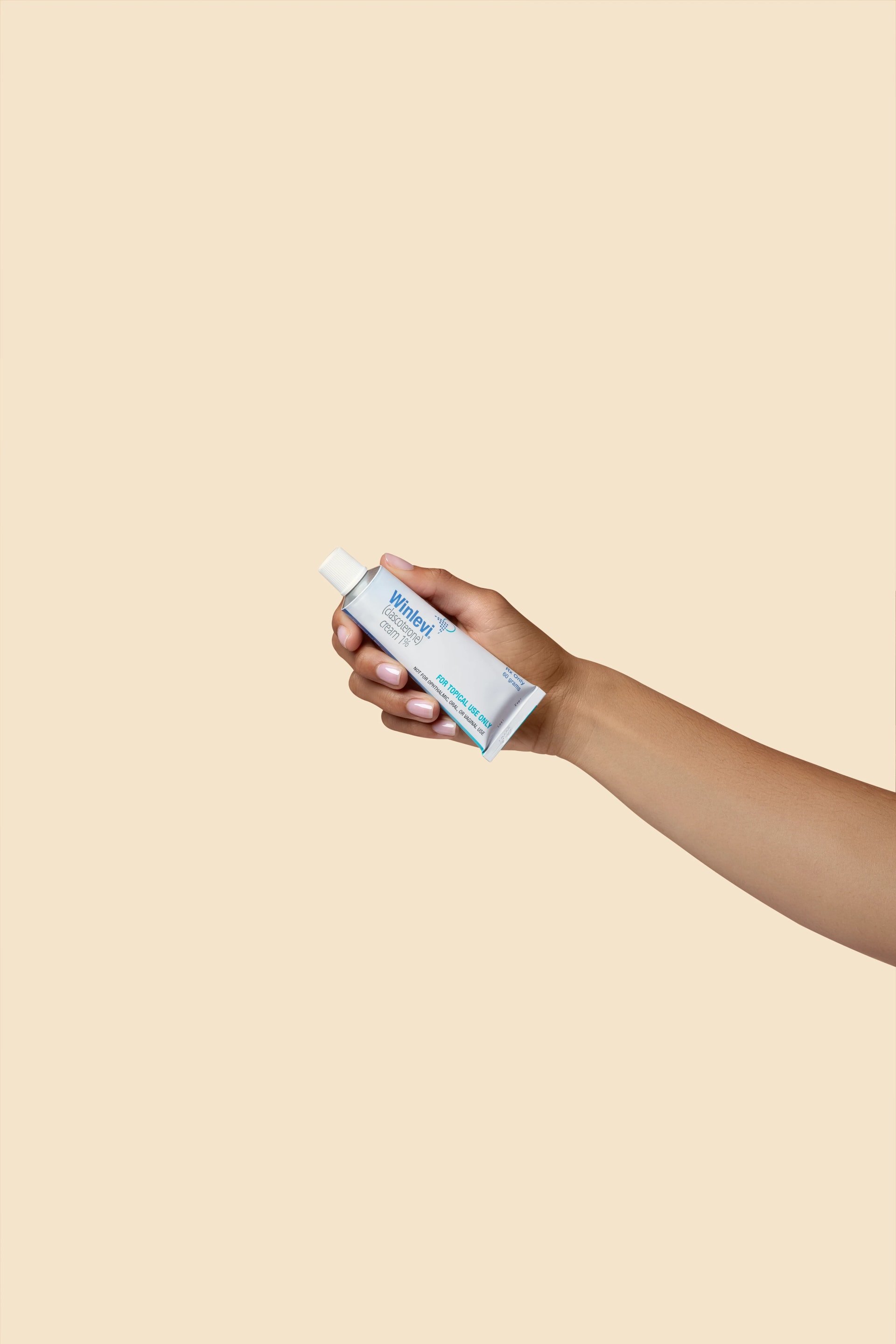 Hand holding tube of Winlevi cream against beige background.