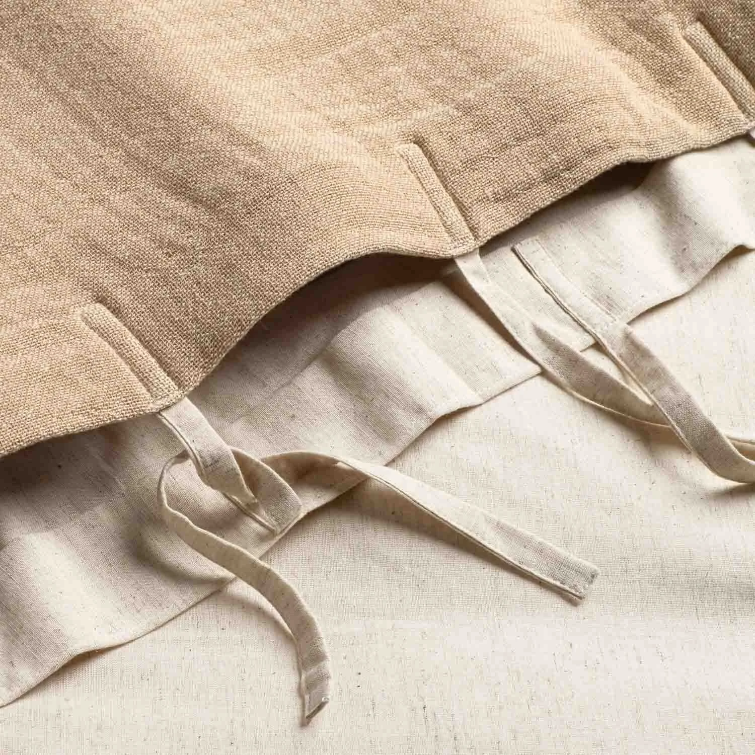 Close-up of beige linen pillowcases with tied fabric closures on a light-colored fabric surface.