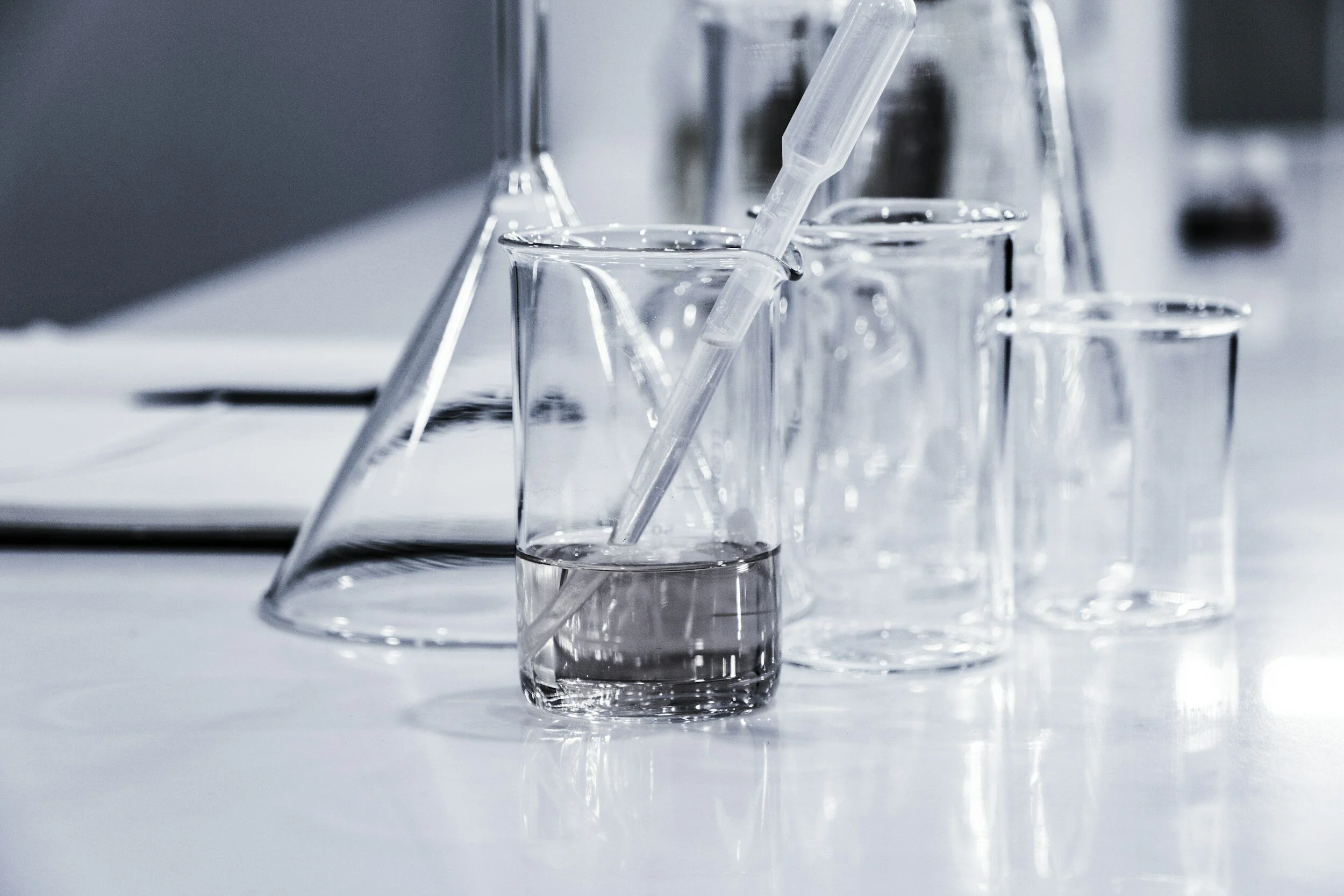A collection of laboratory glassware, including beakers and test tubes, with a pipette in one of the beakers in a clean, bright laboratory setting.