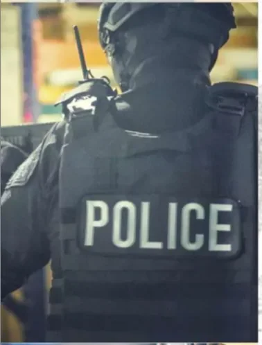 The back of a police officer in tactical gear, wearing a vest labeled “POLICE” and a helmet.