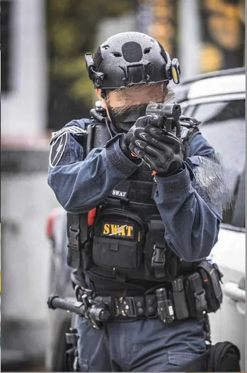 A SWAT team officer aiming a handgun while standing outdoors, wearing tactical gear and a black helmet.
