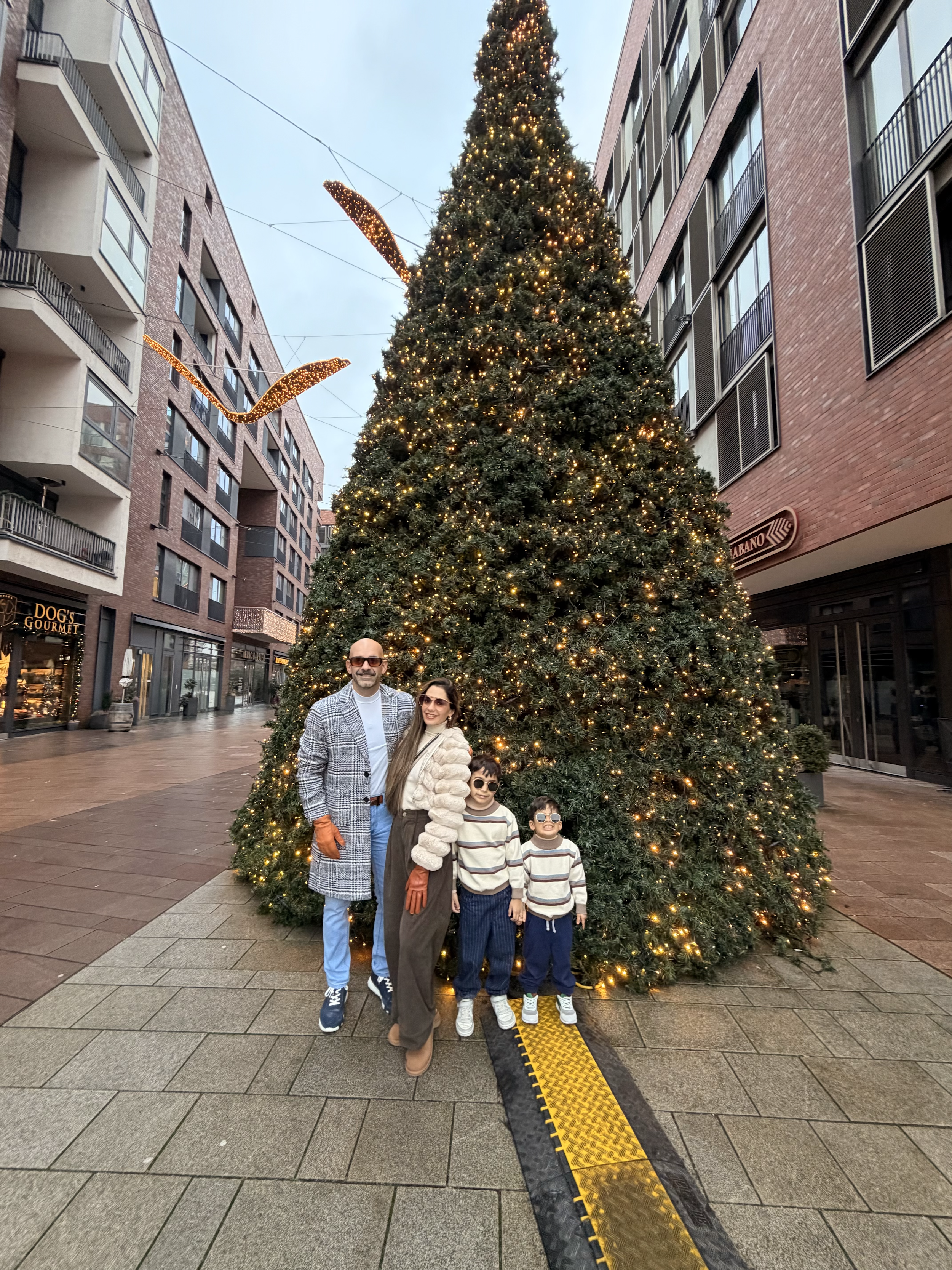 Familia de cuatro personas posando frente a un árbol de Navidad decorado con luces en una calle urbana.
