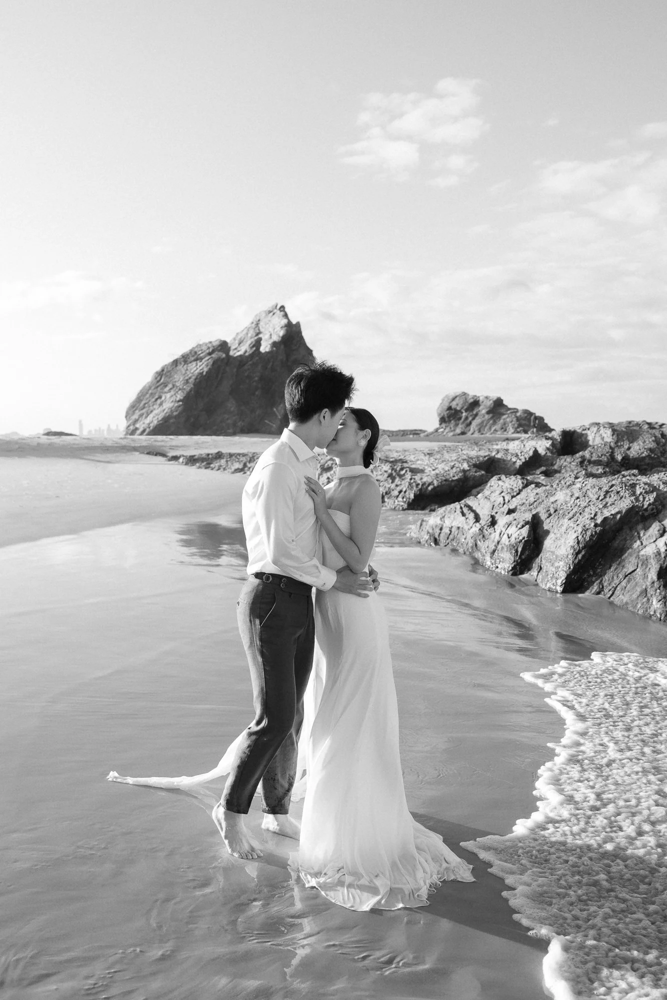 Engaged couple kissing at Currumbin Beach, bride is wearing a flow white dress and groom is wearing a suit