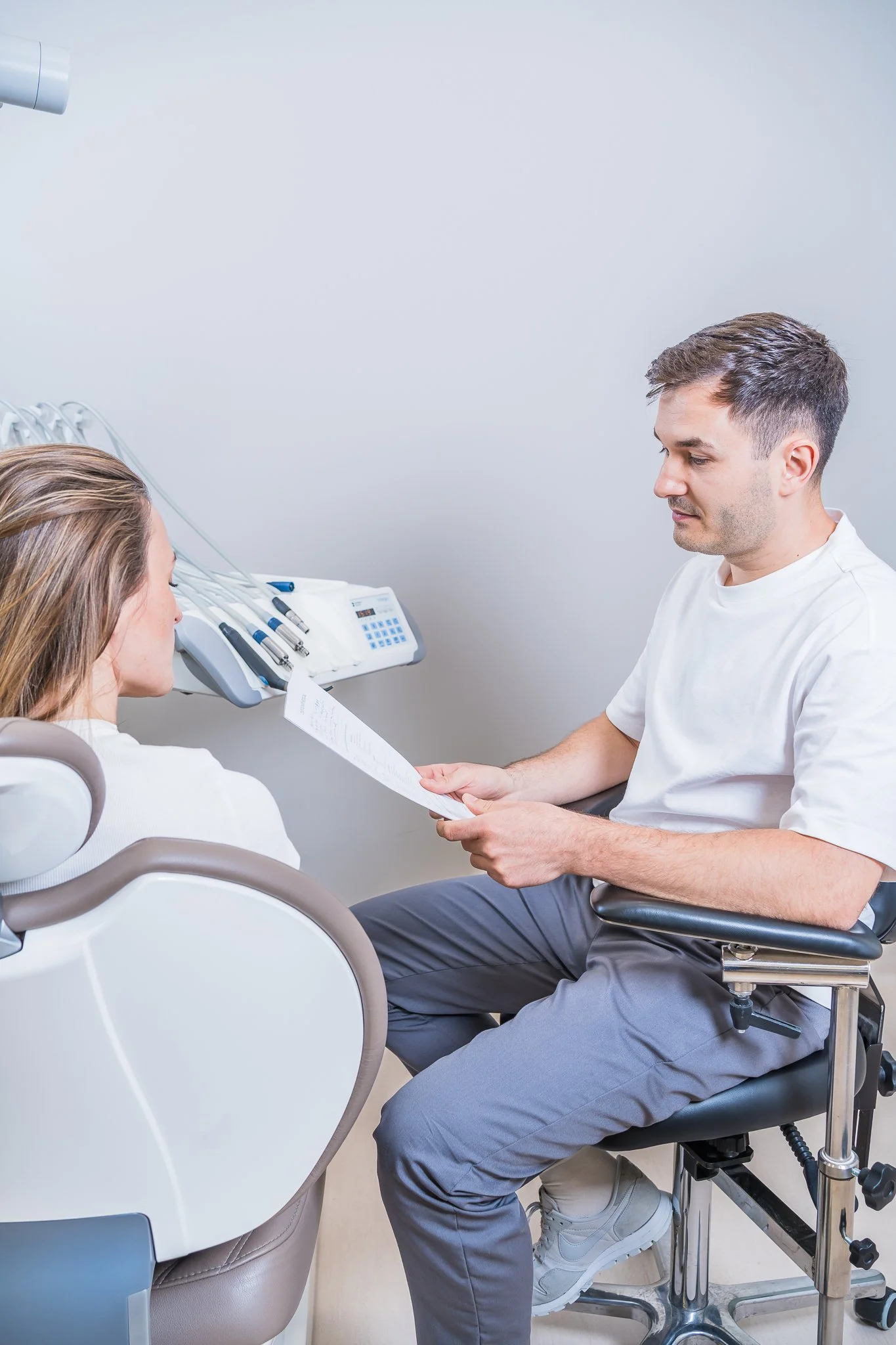 Dentist consulting with a female patient in a dental clinic, sitting in a dental chair, with dental tools and equipment nearby.