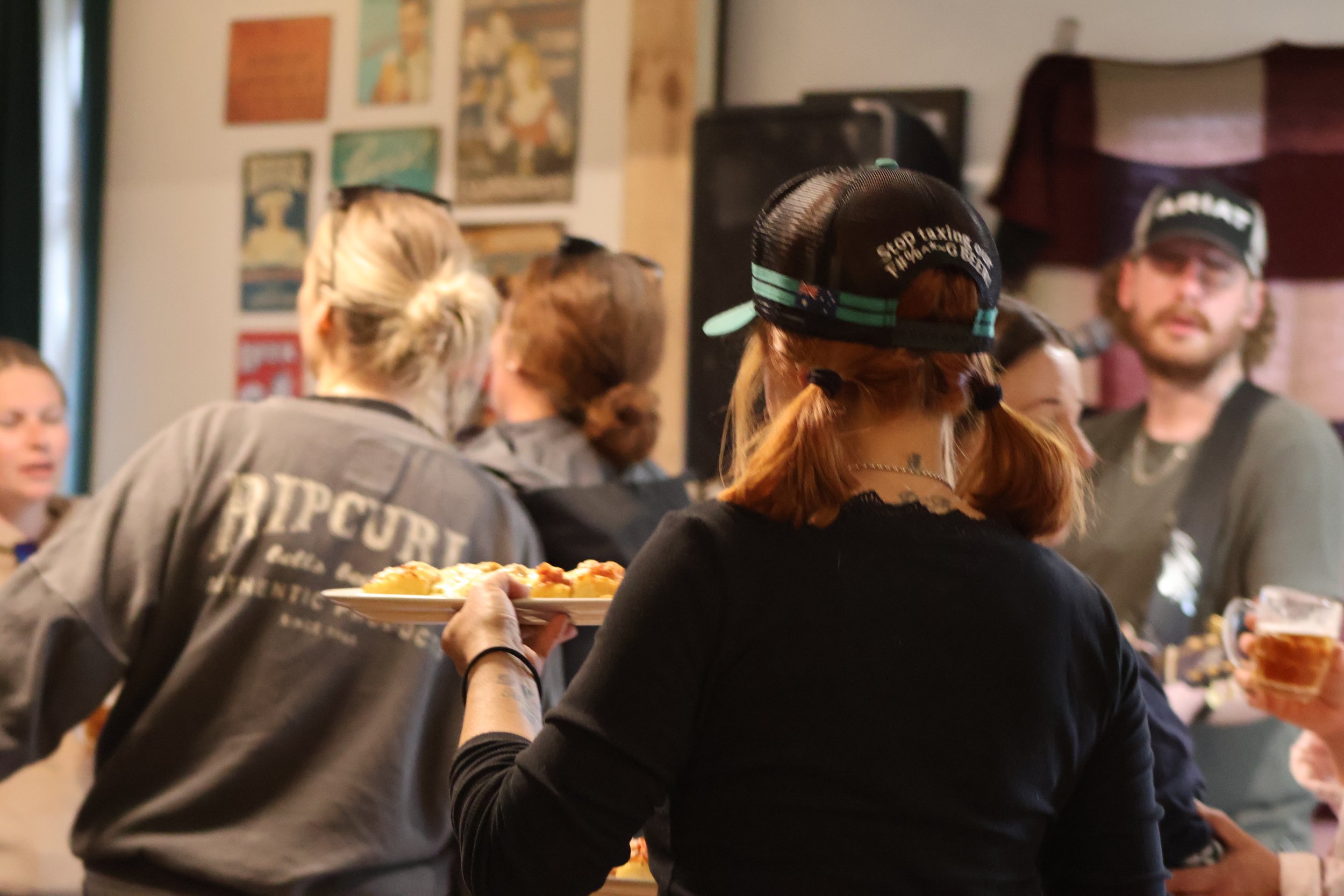 Group of people at a gathering or party, with one person serving pizza on a plate, while others are talking and socializing in a cozy indoor setting.