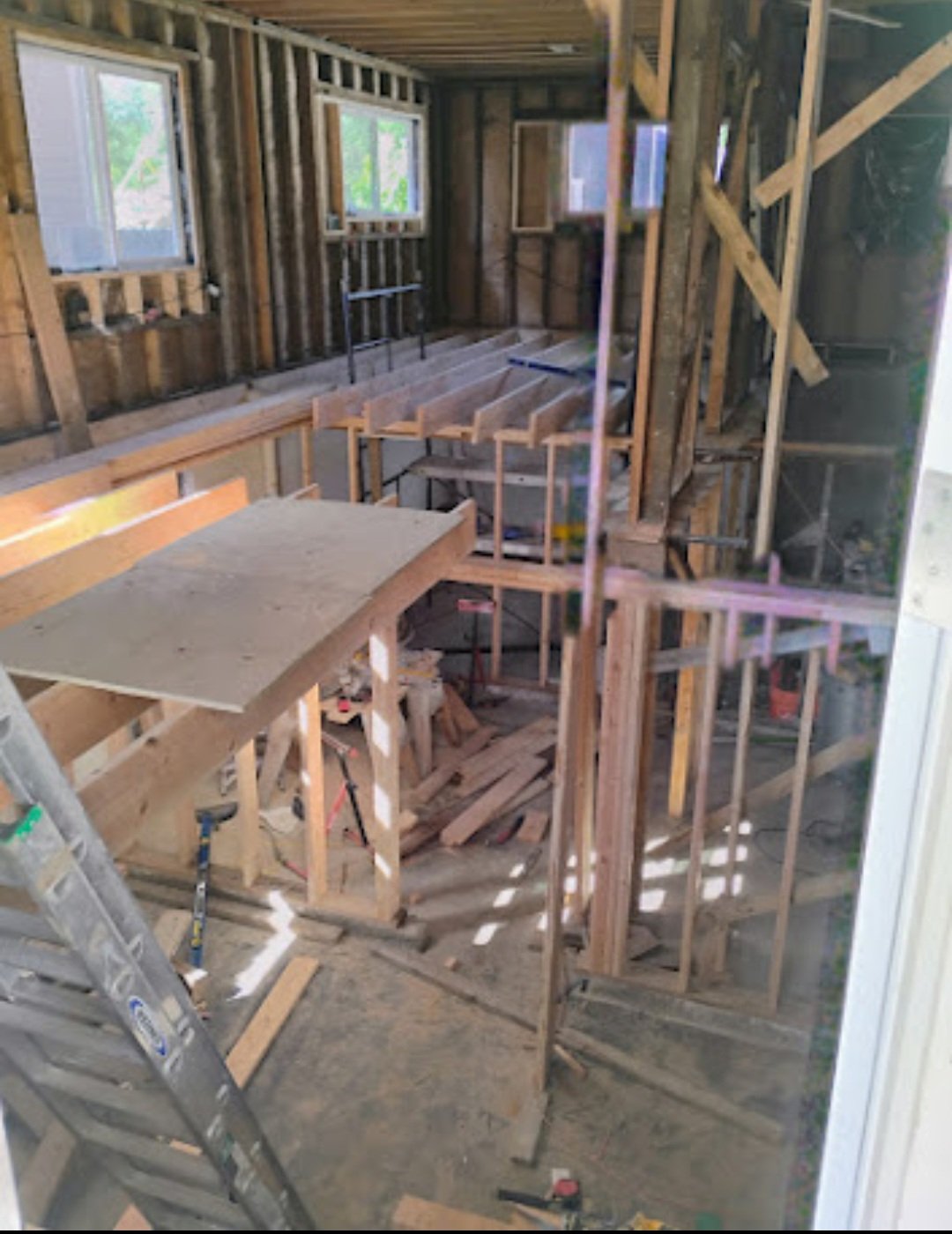 Interior view of a house under construction showing exposed wooden framing, partially installed windows, and construction tools.