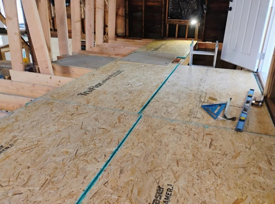 Construction site with plywood flooring, wooden framing, and an open door, indicating an interior phase of building a house.