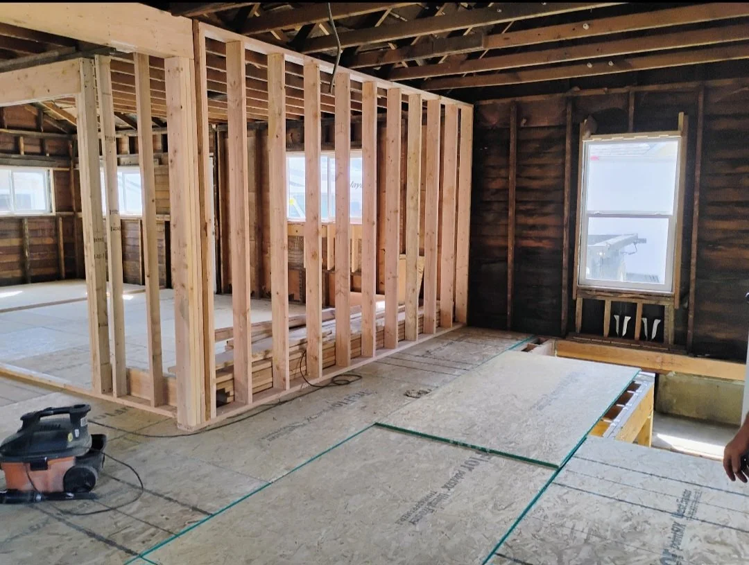 Construction site of a house interior with exposed wooden framing and insulation, unfinished walls, and windows.