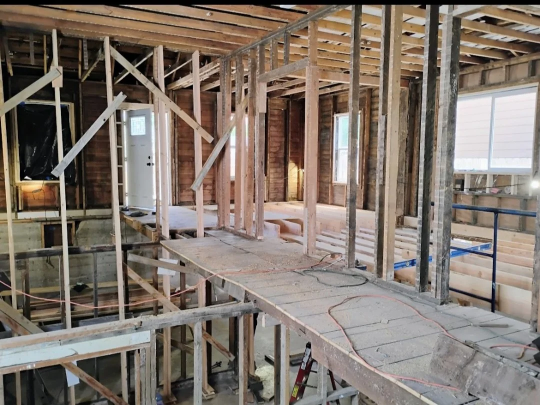 Interior of a house under construction with exposed wooden framing, scaffolding, and a temporary walkway.