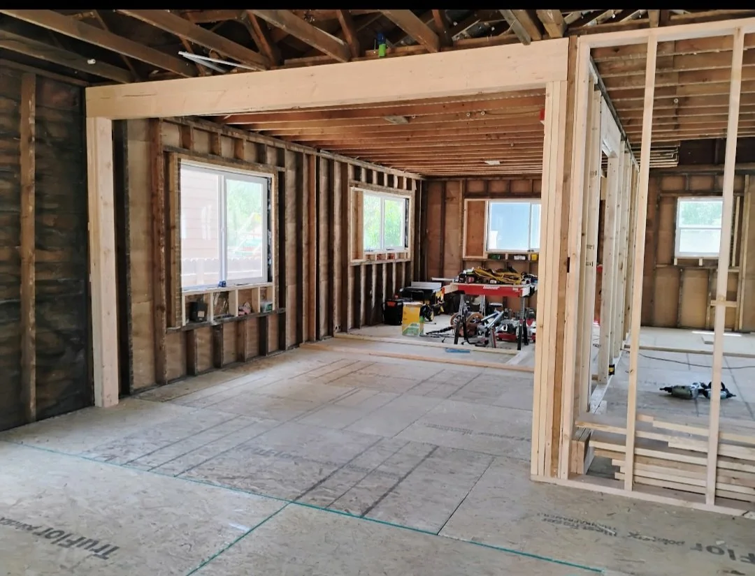 Interior of a house under construction with exposed wooden framing, windows, and construction tools and materials inside.