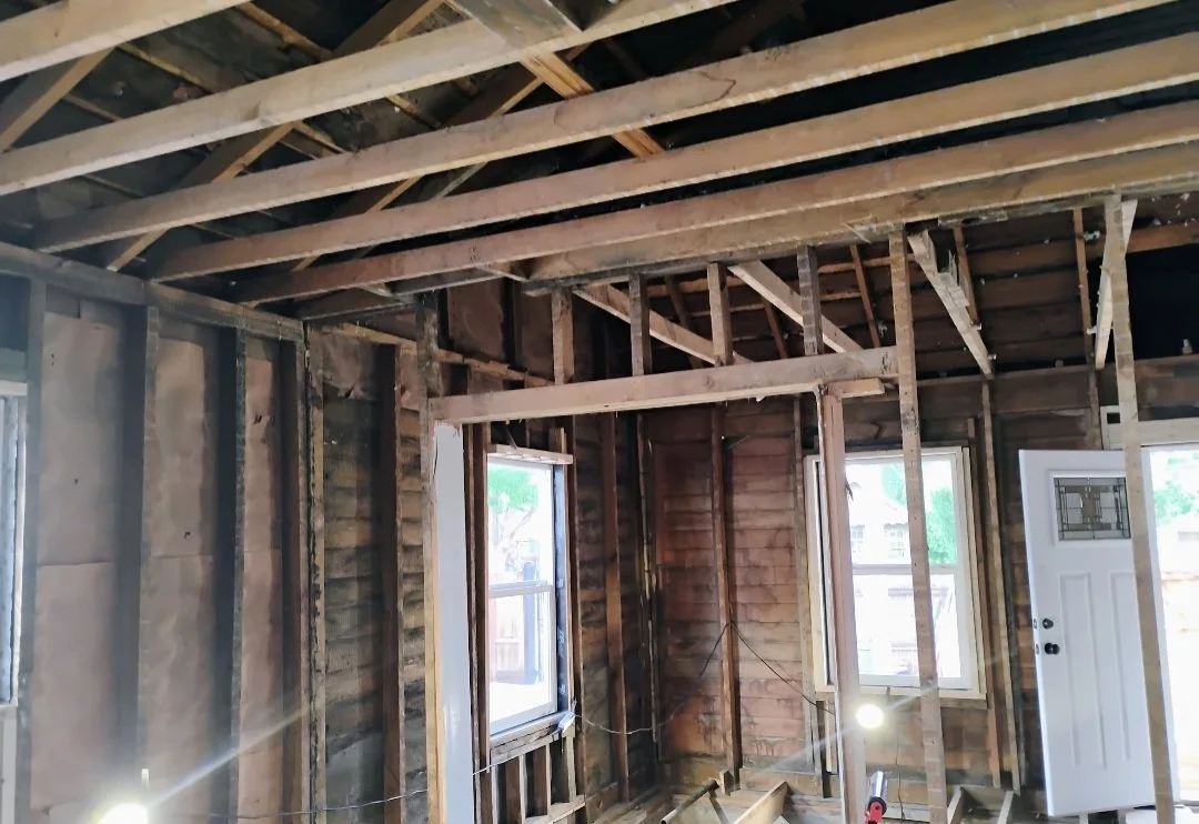 Interior of a house under renovation with exposed wooden framing, two windows, and a door.