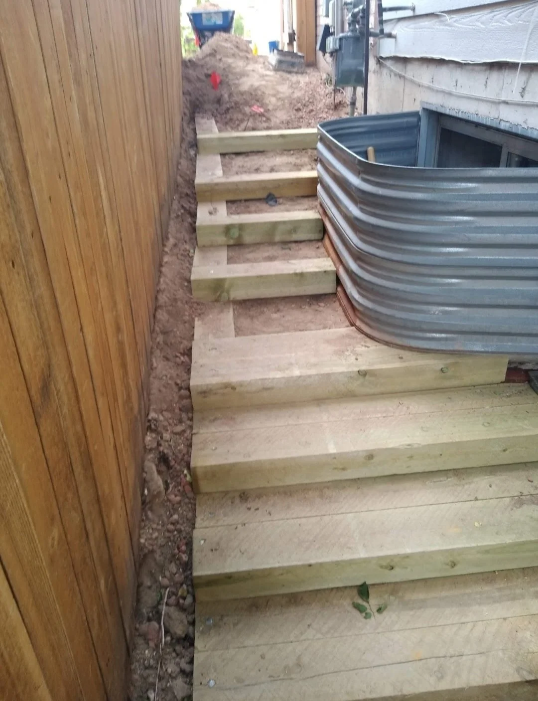 New wooden deck with stairs being built beside a house, with dirt and construction materials around.