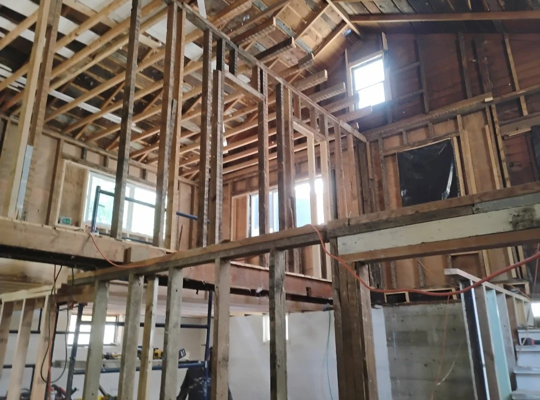 Interior of a house under construction with exposed wooden framing, new windows, and visible roof trusses.