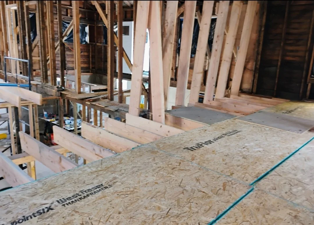View of a building under construction showing wooden framing, plywood flooring, and construction materials inside.