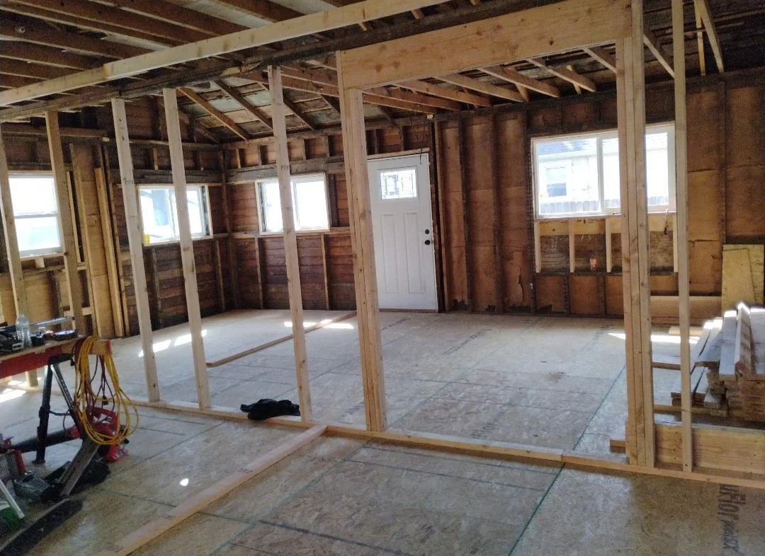 Interior of a house under construction with exposed wooden framing, unfinished walls, and a door leading outside.