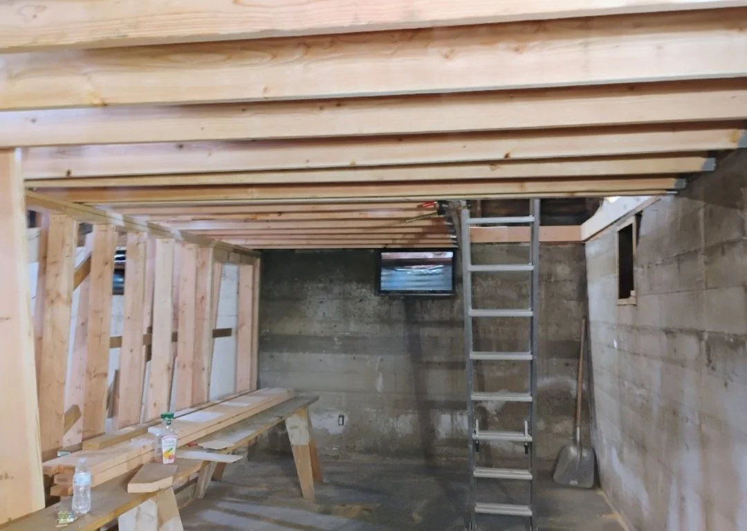 Interior of a construction site with wooden framing, a metal ladder, and concrete block walls.