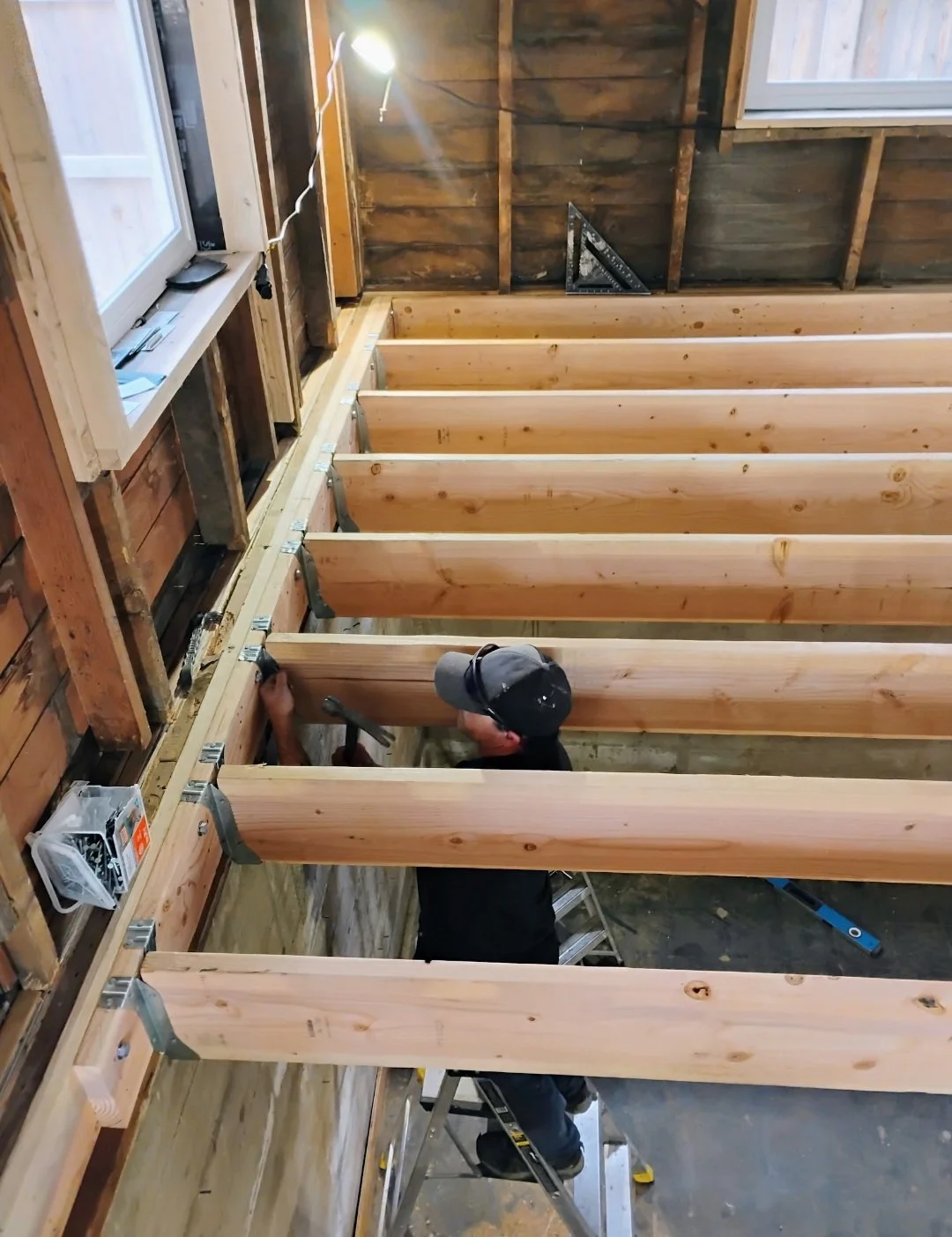 A man working on a wooden framing project inside a partially built room, with wooden beams and insulation visible in the walls.