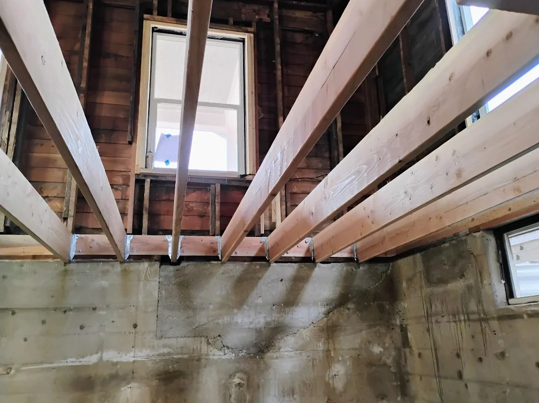 Interior of a building under construction with wooden framing and a small window in the wall.