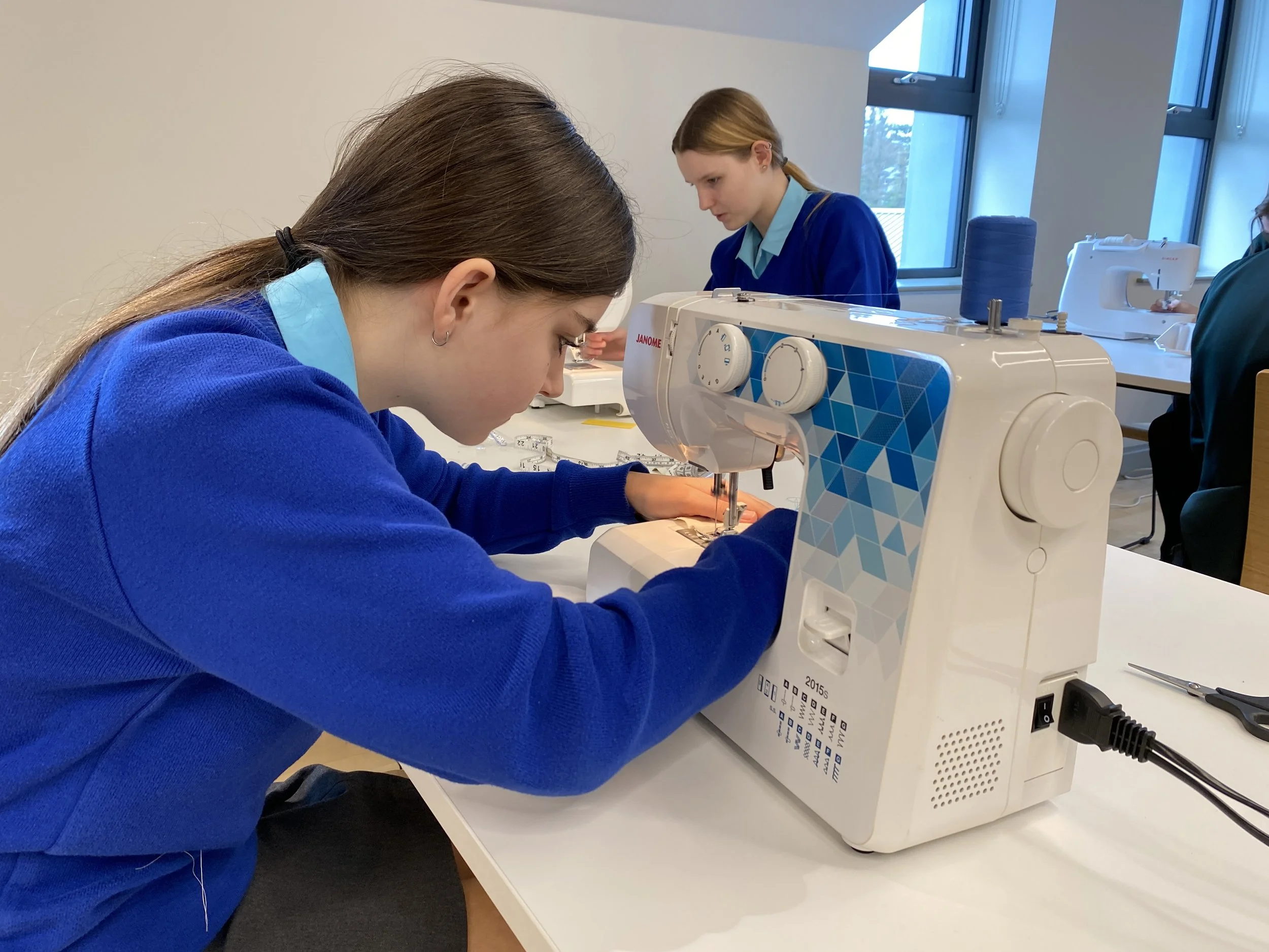 A girl in a blue jumper using a sewing machine