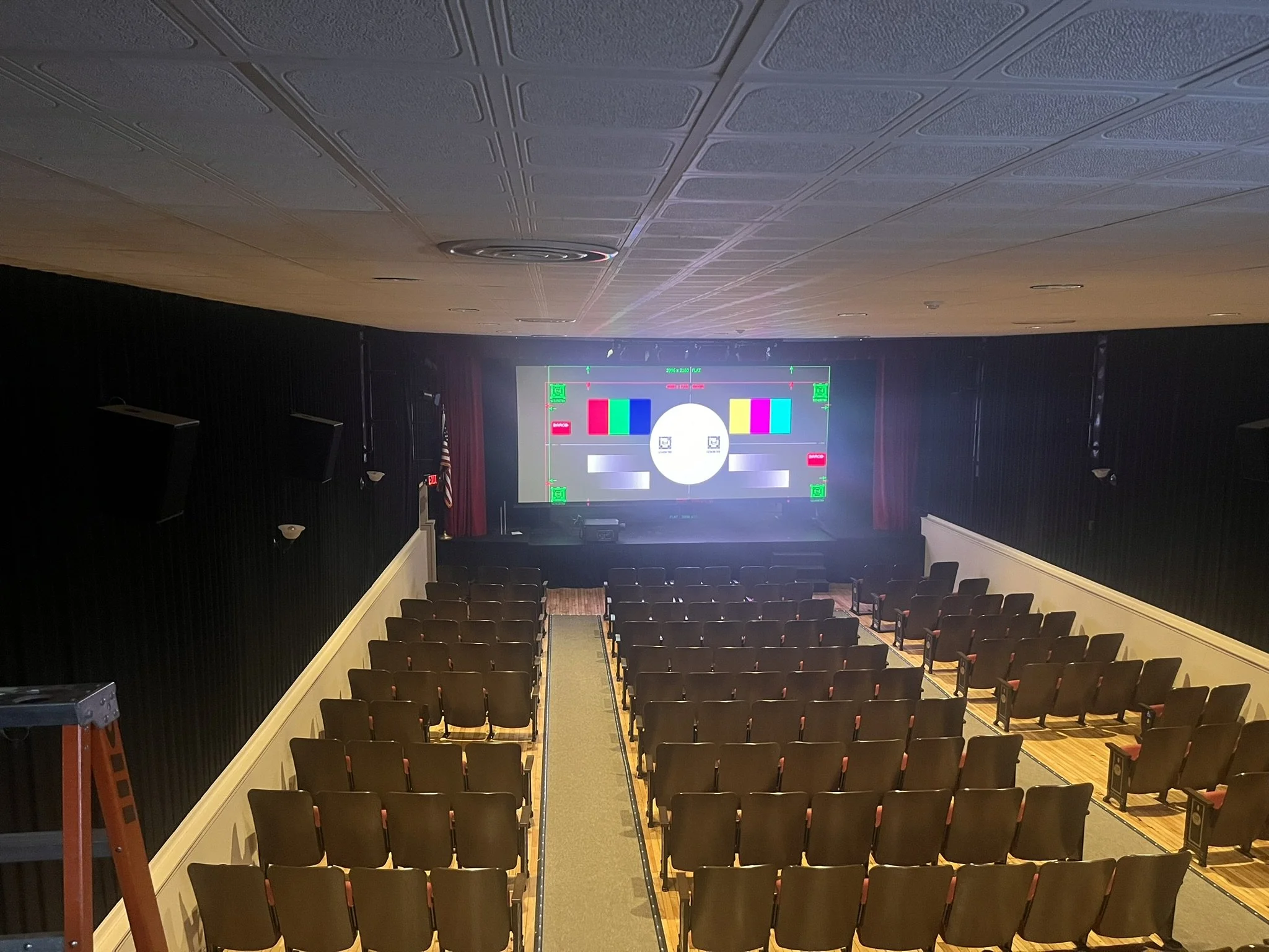 Empty theater with rows of seats facing a large screen displaying a test pattern to calibrate the new projector.