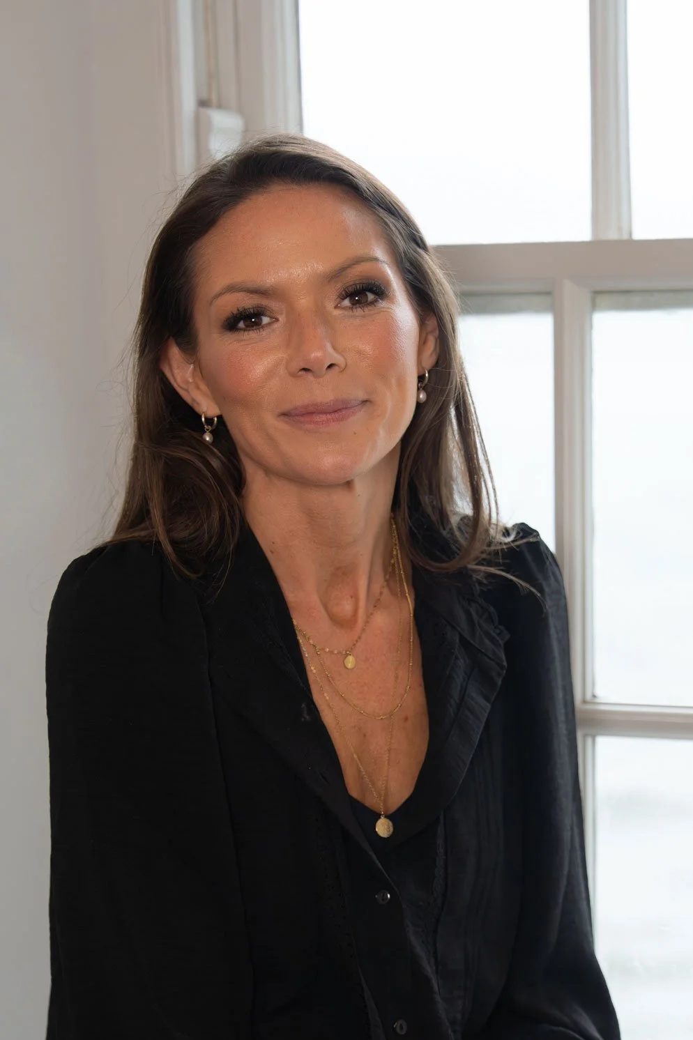 Makeup artist Hannah, wearing a black top, standing in front of a window with white frames.