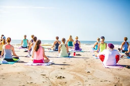 Students enjoying a community beach yoga class on Folly Beach in South Carolina. Walk ins are welcome and all levels and ages are encouraged to join.
