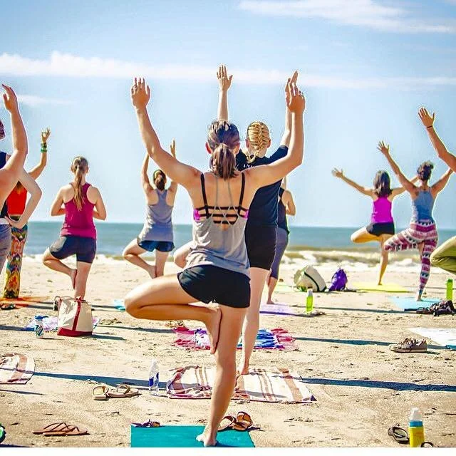 Participants practicing community beach yoga on Folly Beach in Charleston, South Carolina during an outdoor yoga class.