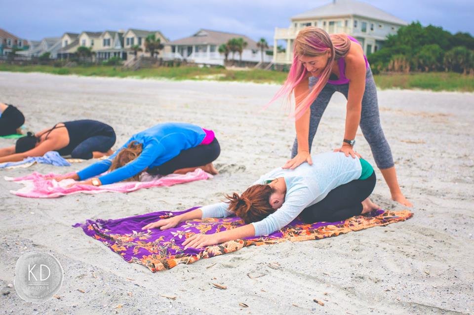 Serenity Tree Yoga instructor offering a gentle hands-on assist during an outdoor beach yoga class in Charleston, South Carolina.