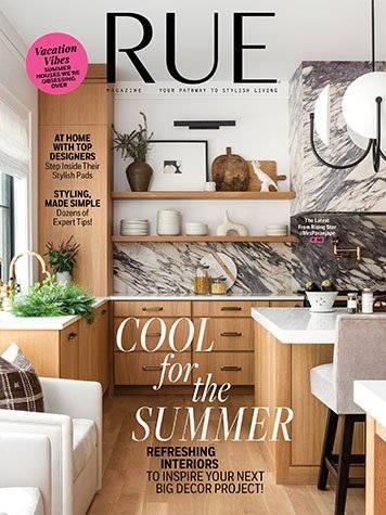 Cover of RUE magazine featuring a modern kitchen with wooden cabinets, white open shelves, marble backsplash, and a white farmhouse sink. Decor includes plants, vases, and kitchenware. Text on cover promotes summer decor ideas and stylish home interiors.