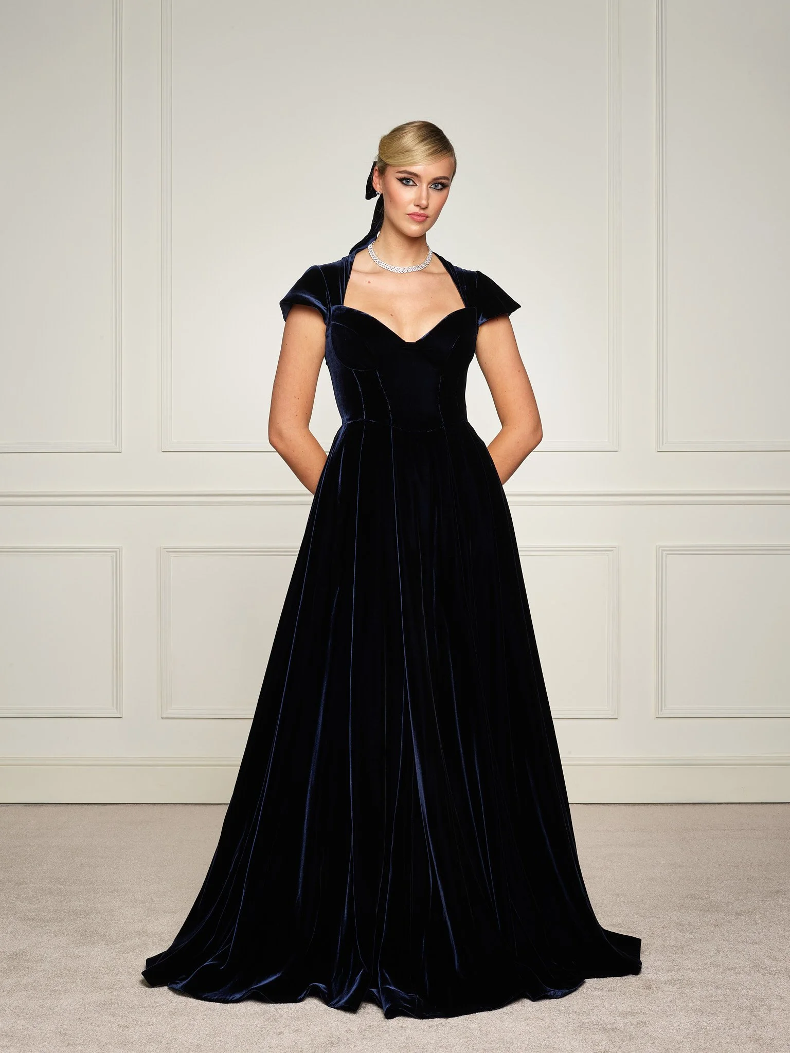 Paget London navy velvet gown photographed from the front, showcasing structured neckline, cap sleeves, and floor-length silhouette