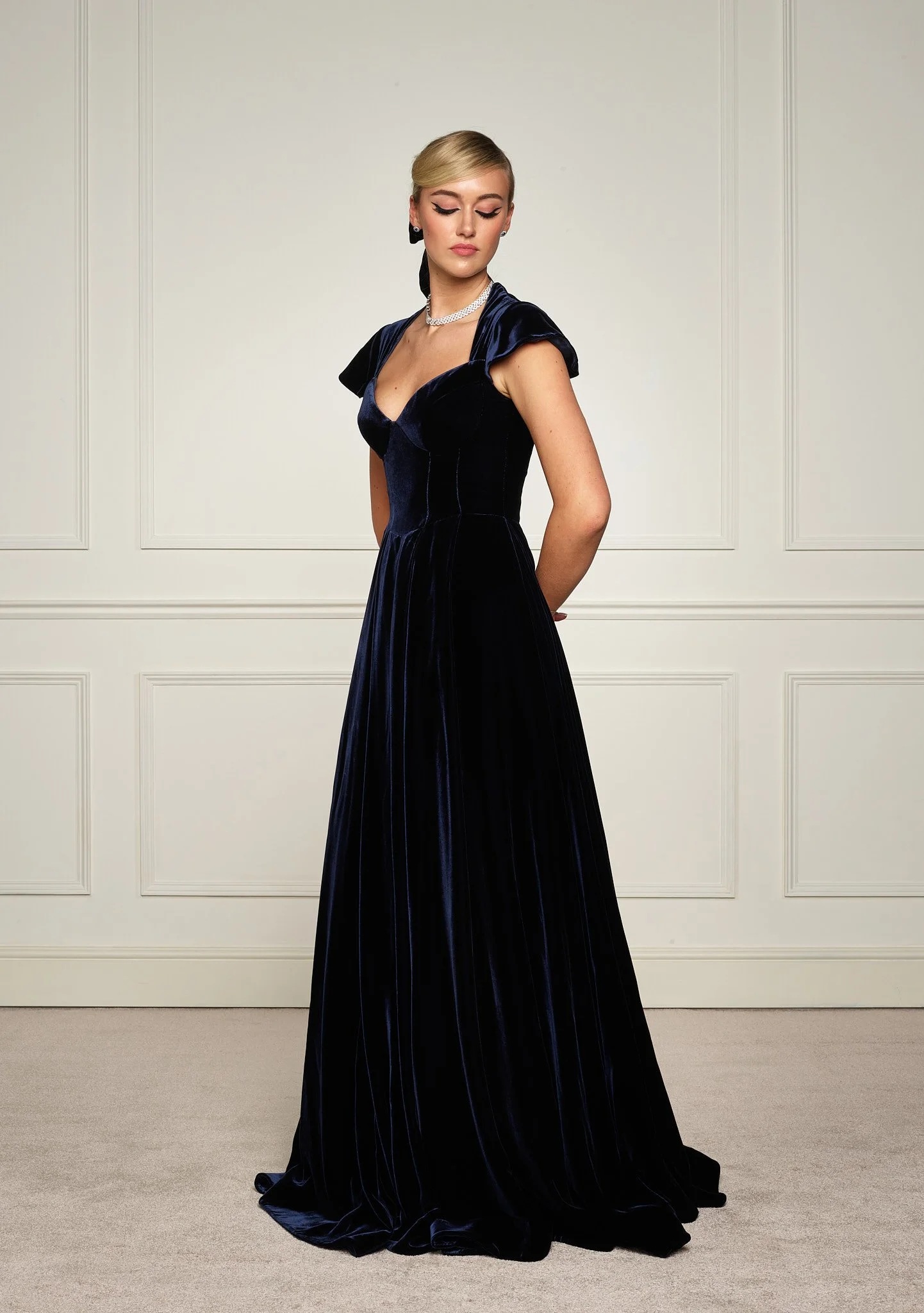 Navy velvet evening gown by Paget London, angled studio view highlighting sculpted bodice and flowing full-length skirt