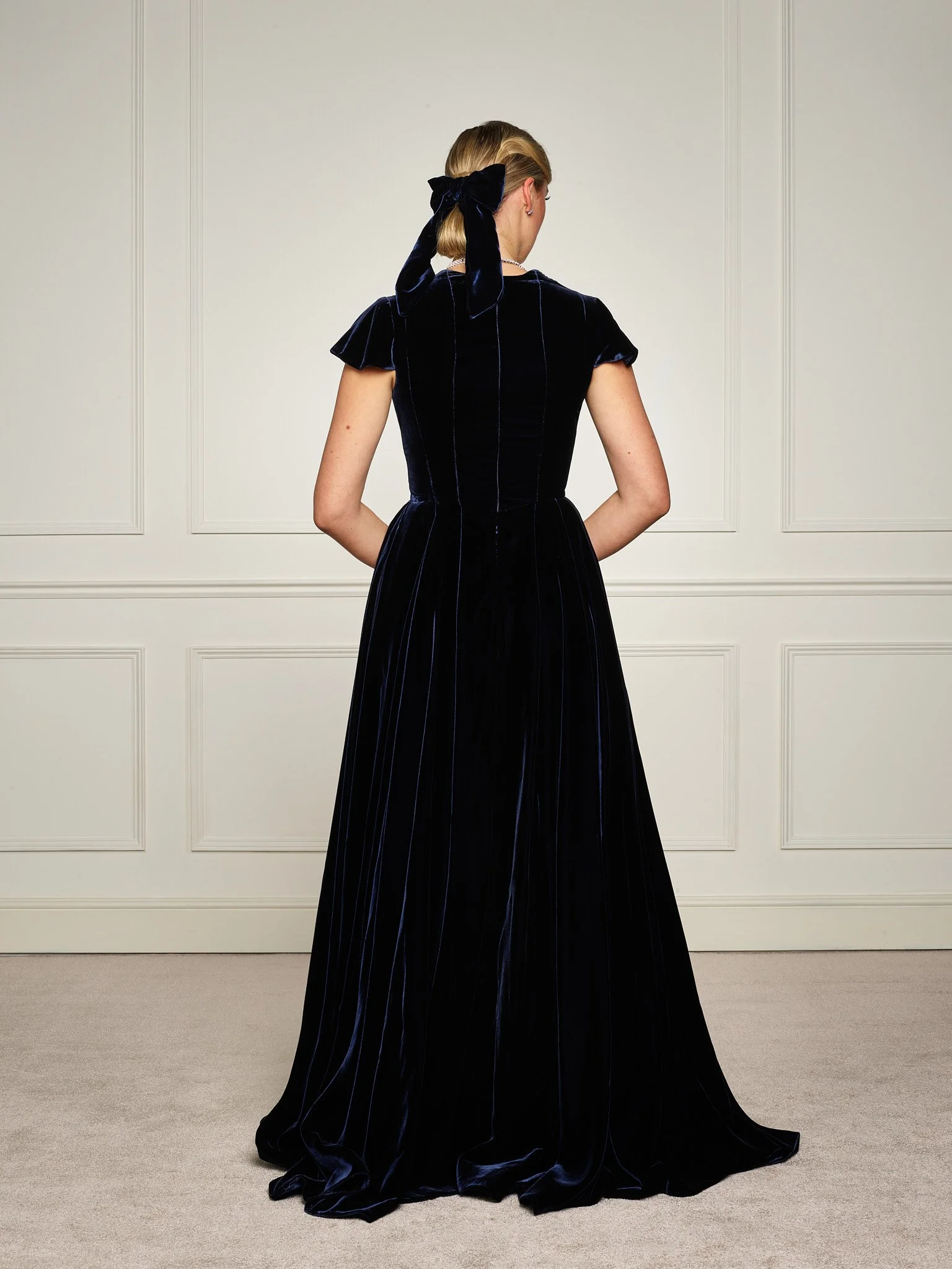 Back view of Paget London navy velvet evening gown, revealing fitted waist, elegant back detailing, and flowing velvet skirt