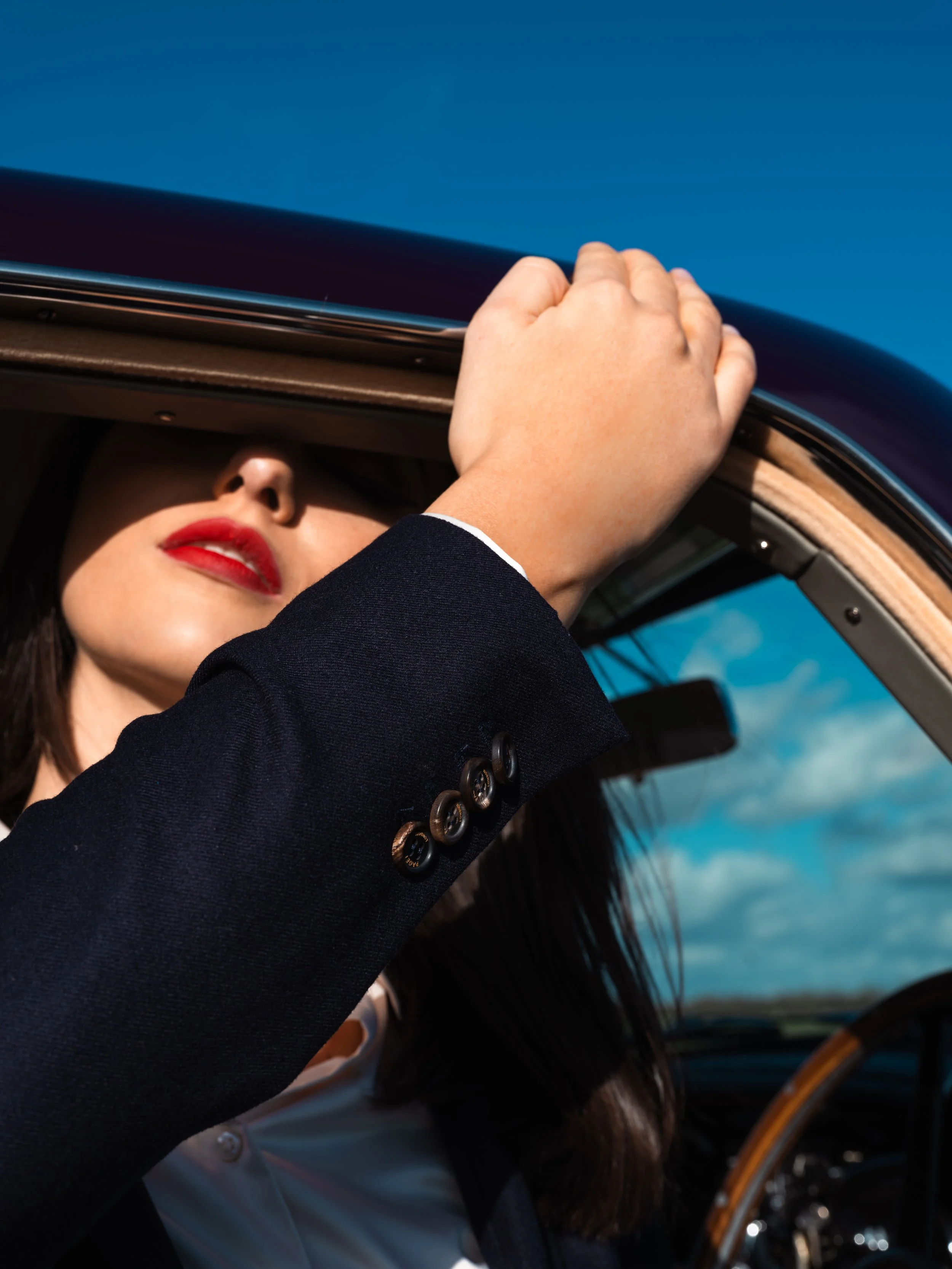 Detail of a navy women’s tailored suit by Paget London, showing structured wool blazer sleeve and buttons styled inside a classic car.