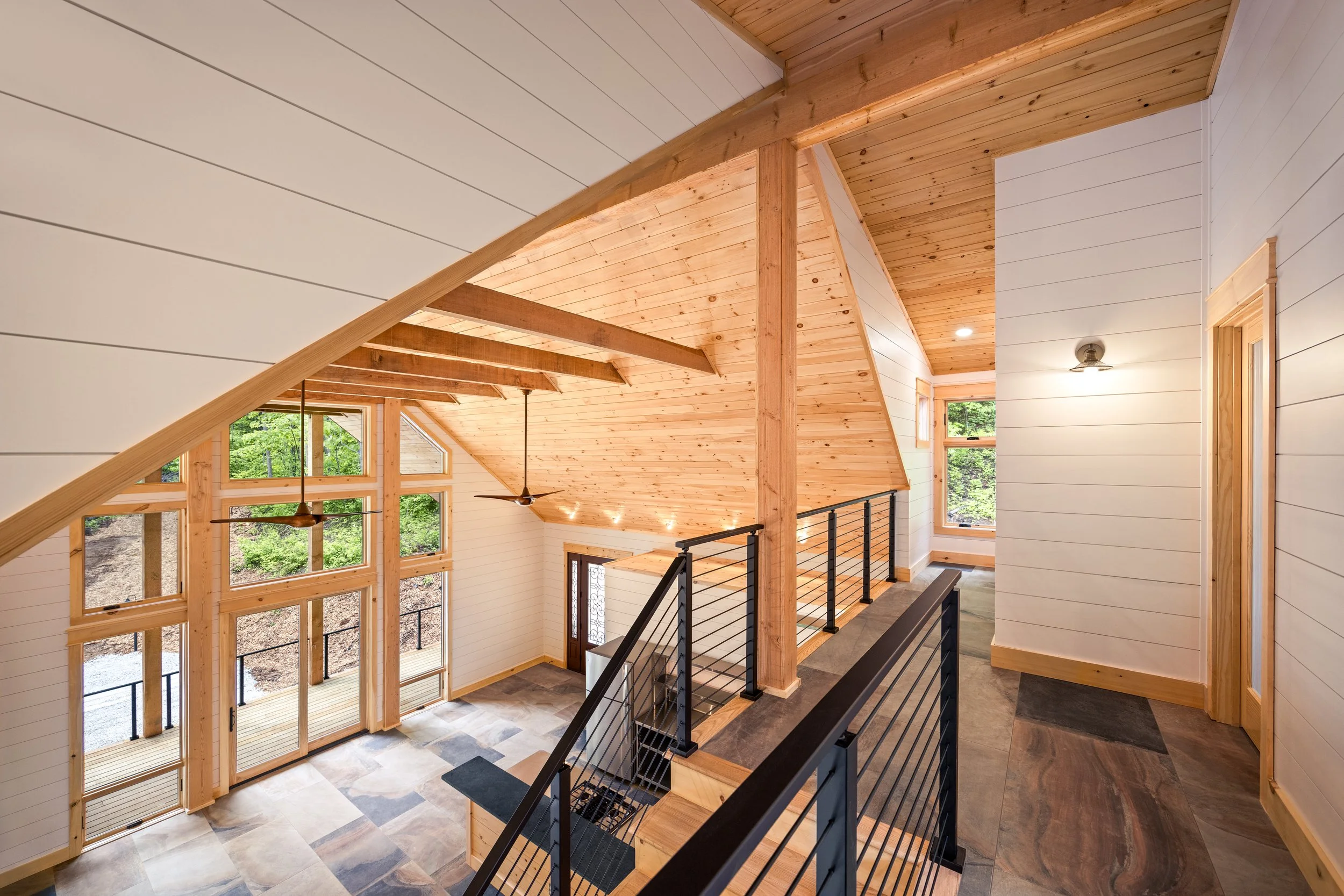 Loft overlooking the great room with modern cable railing, exposed timber framing, and Blue Ridge Mountain panoramic views through expansive windows.