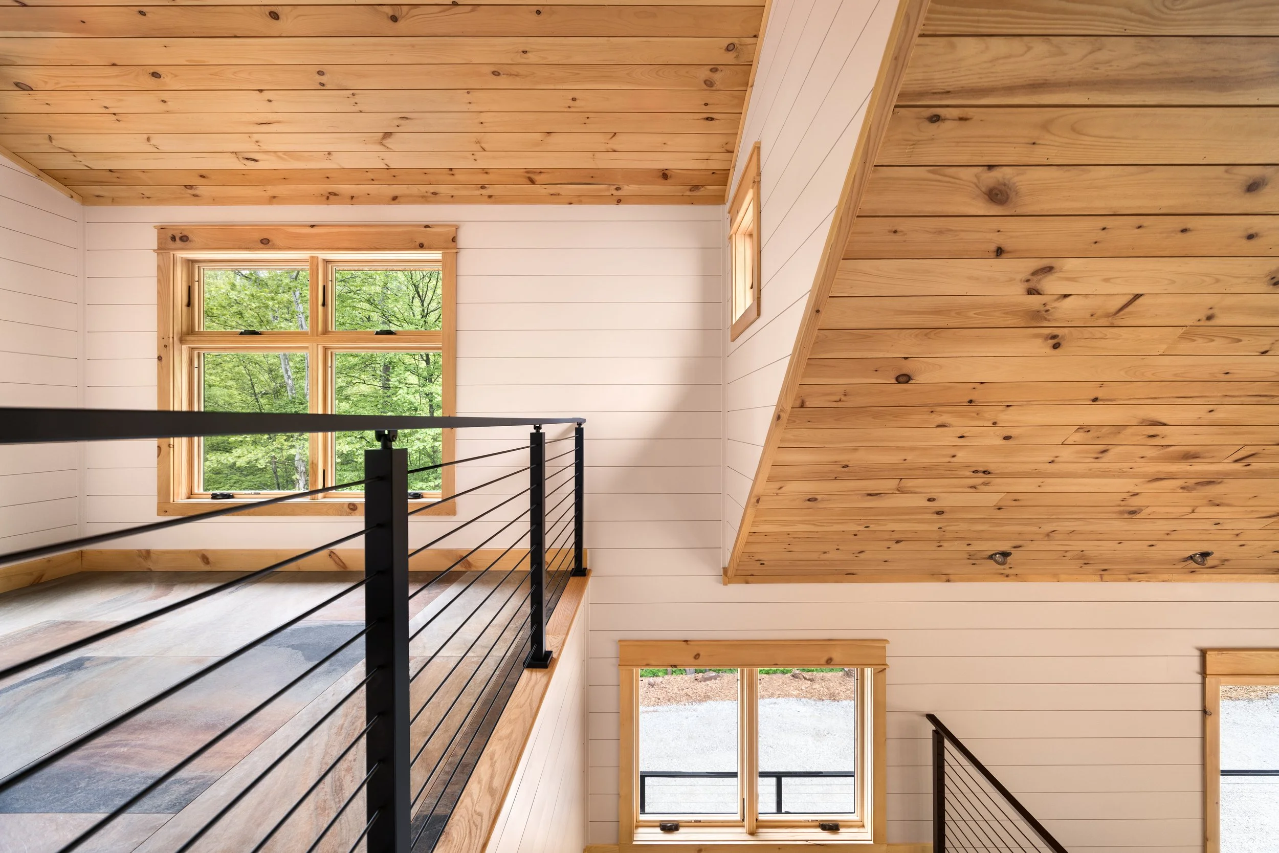 Upper loft with custom cable railing, vaulted wood ceilings, white shiplap walls, and expansive windows showcasing the clean lines and craftsmanship of a custom mountain home in Nelson County, Virginia.