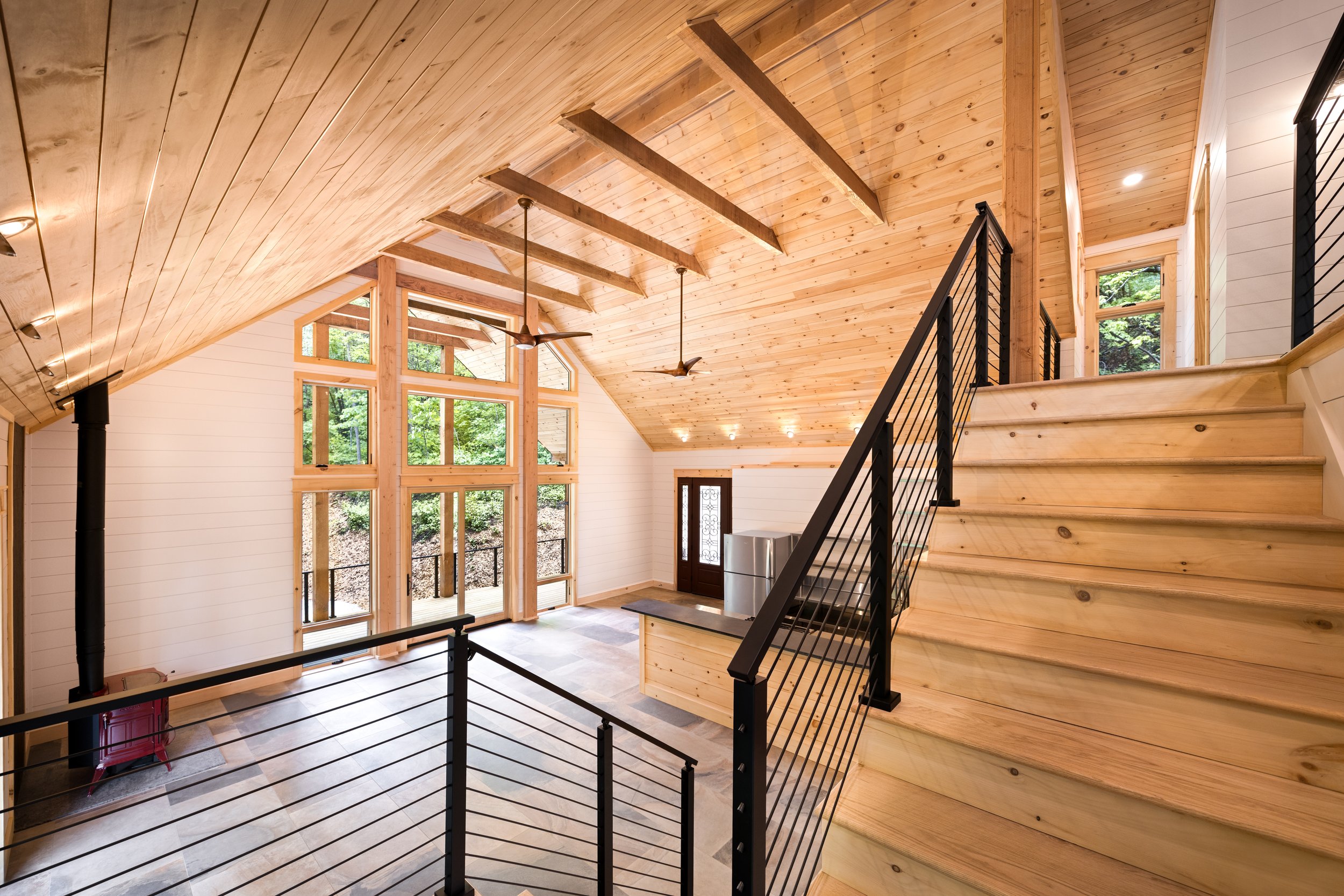 Loft overlooking the great room with modern cable railing, exposed timber framing, and Blue Ridge Mountain panoramic views through expansive windows.