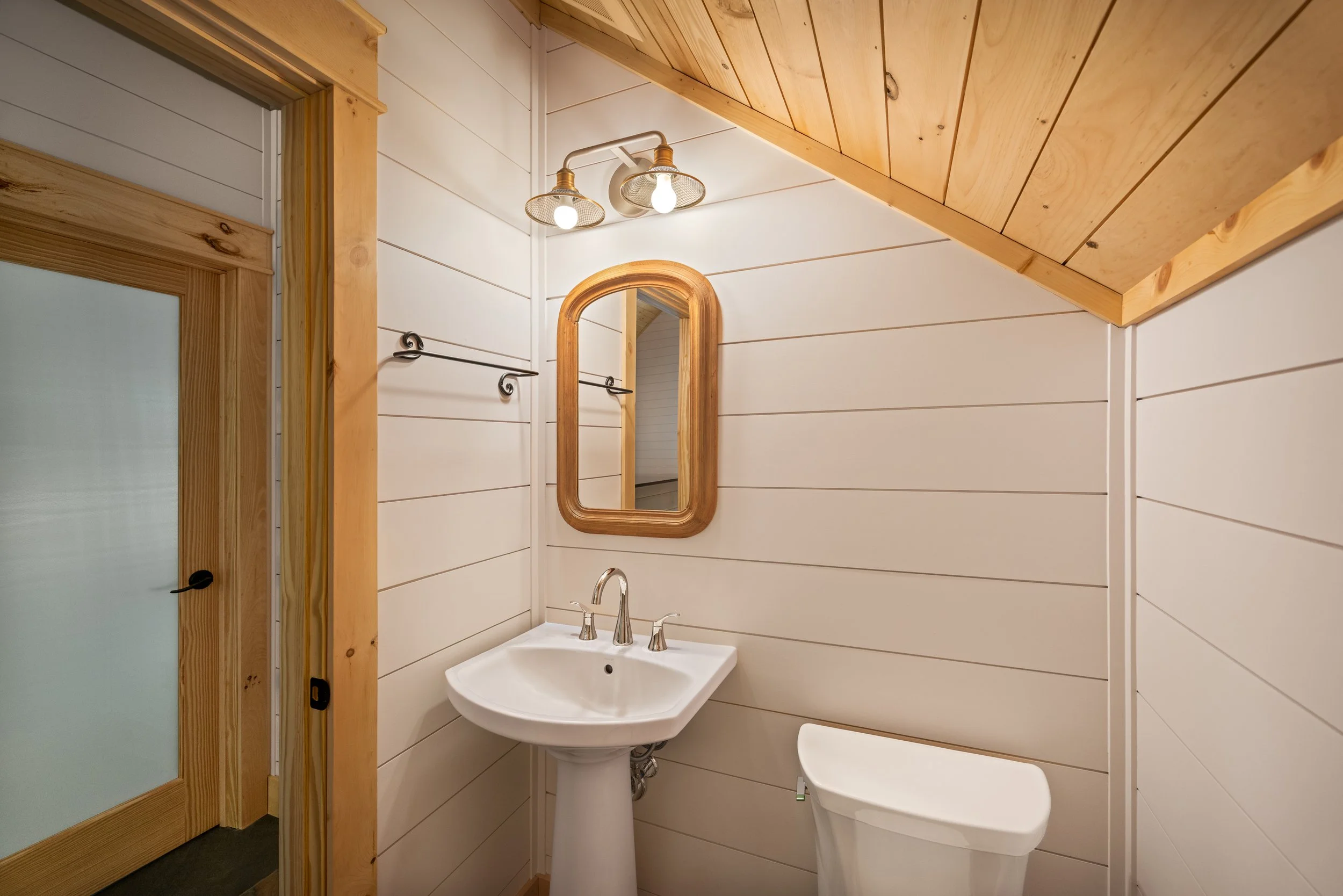 Half bathroom featuring white shiplap walls, a tongue-and-groove wood ceiling, natural wood trim, a pedestal sink in a custom mountain home in Nelson County, Virginia.