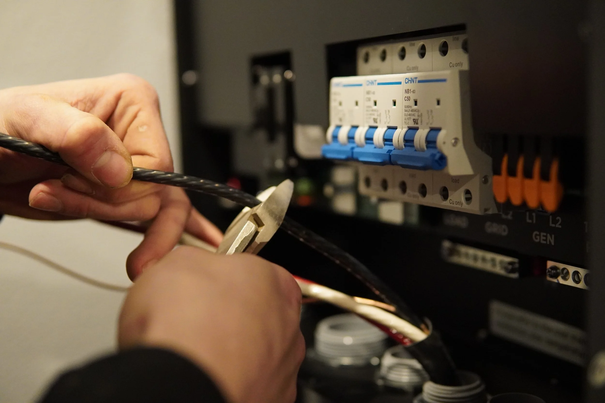 A person working on an electrical panel, connecting or repairing electrical wires with a tool.