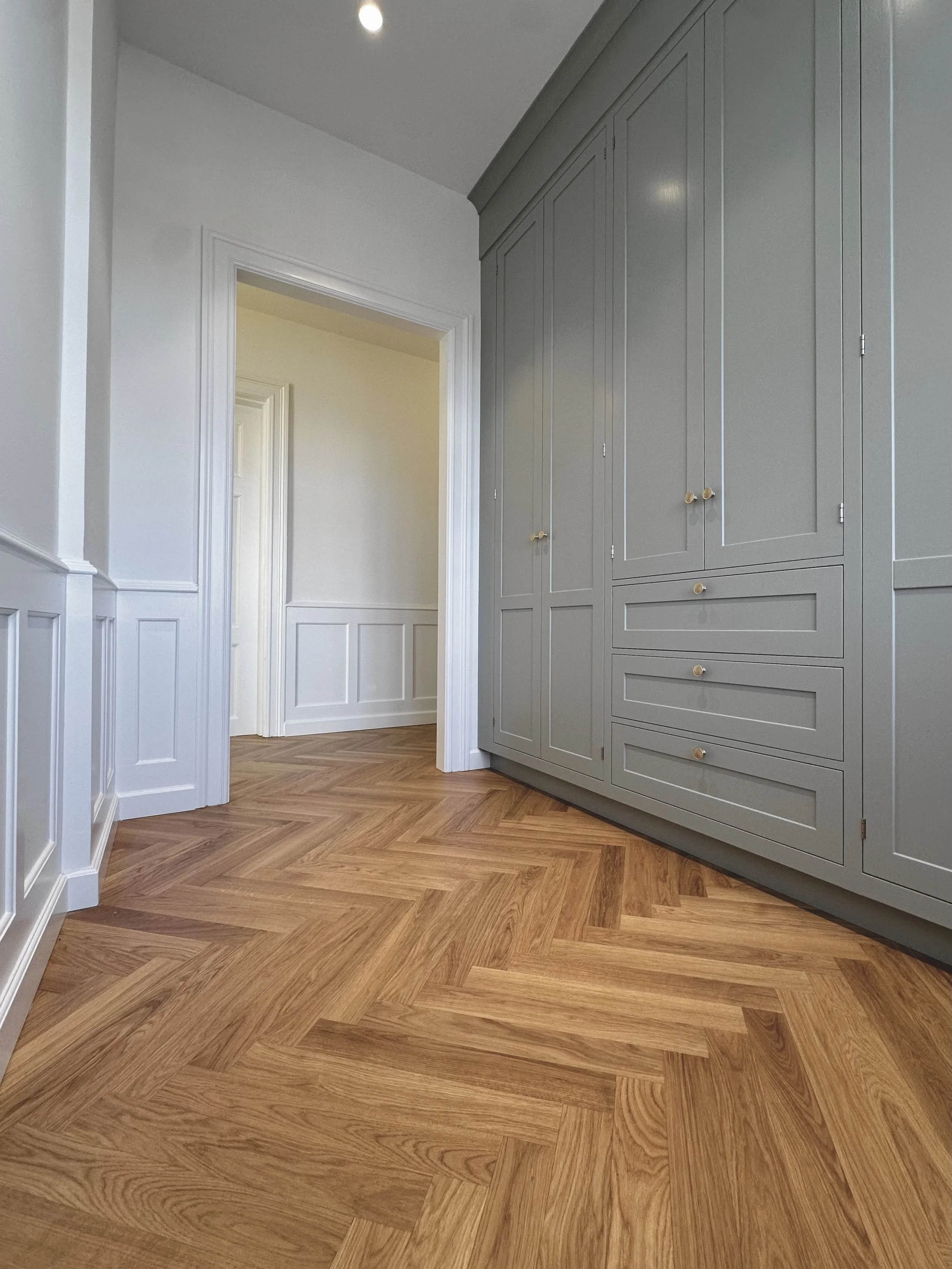 Interior view of a room with light gray built-in cabinets and wood herringbone patterned flooring.