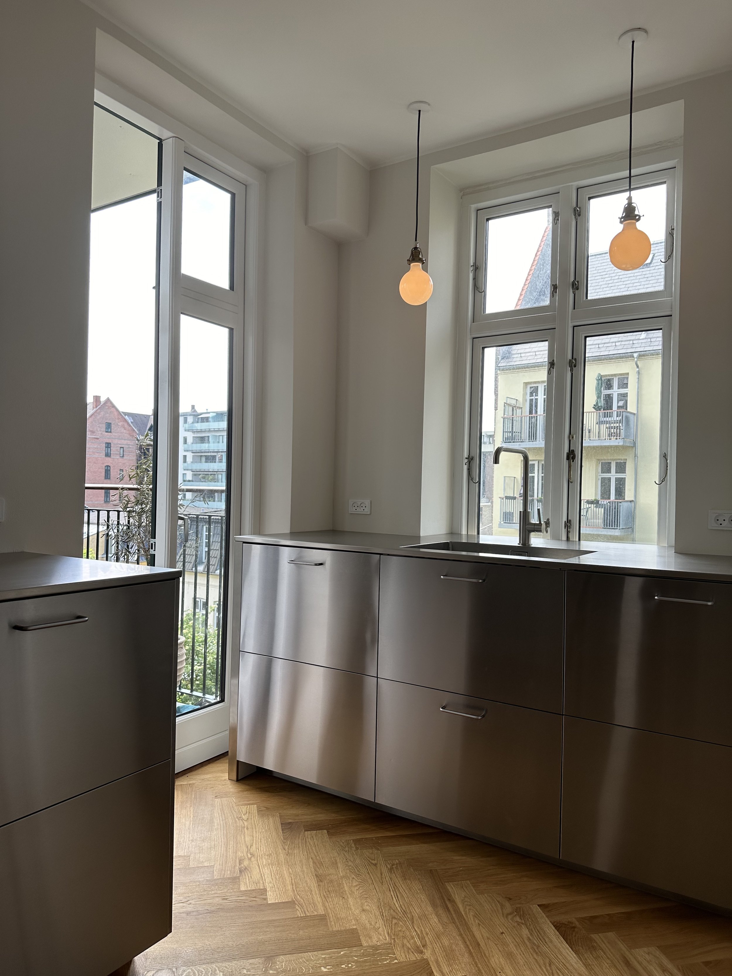Modern kitchen with large windows, wooden flooring, and beige cabinets.