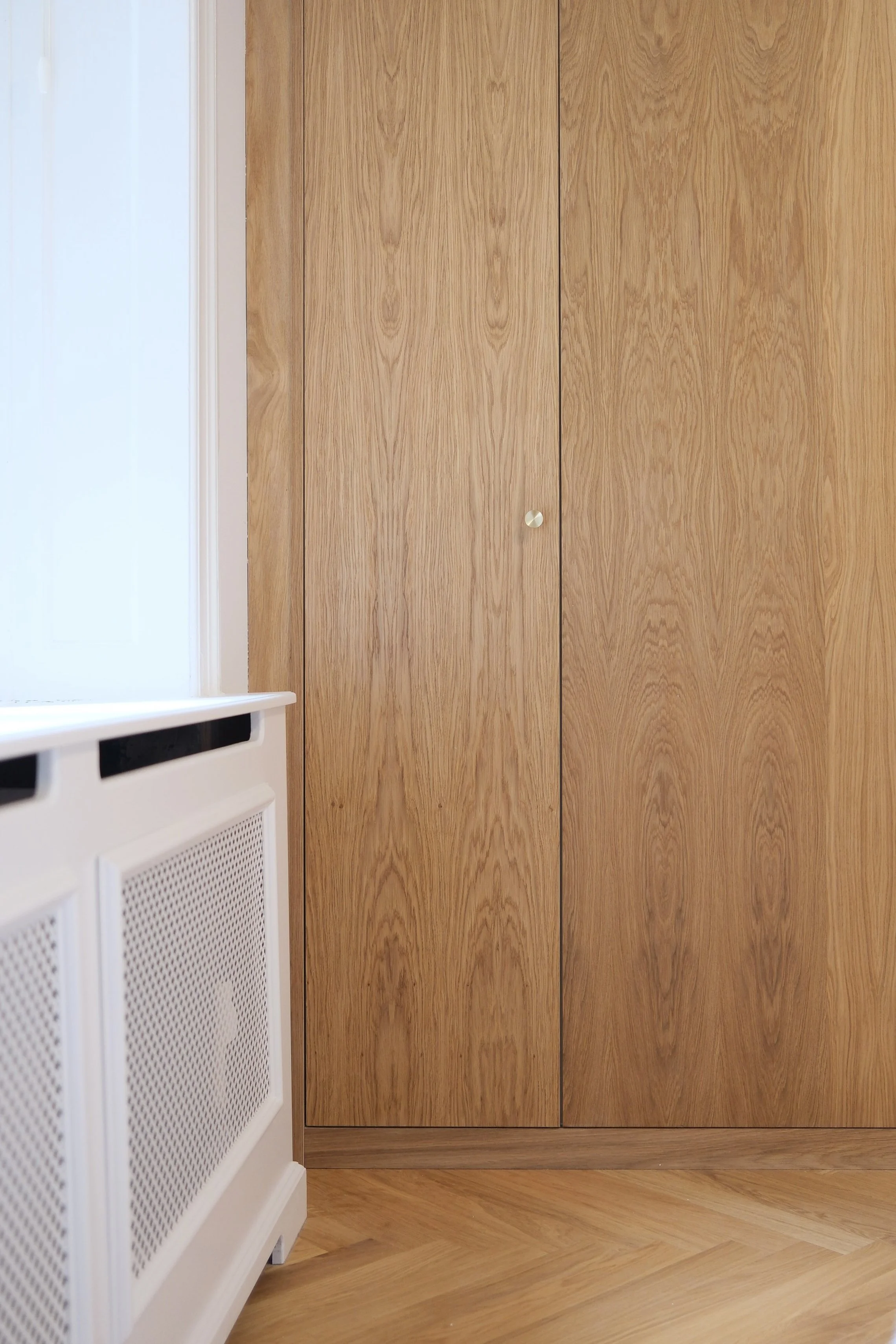 Wooden closet doors adjacent to a white vent cover on a light-colored floor and wall.