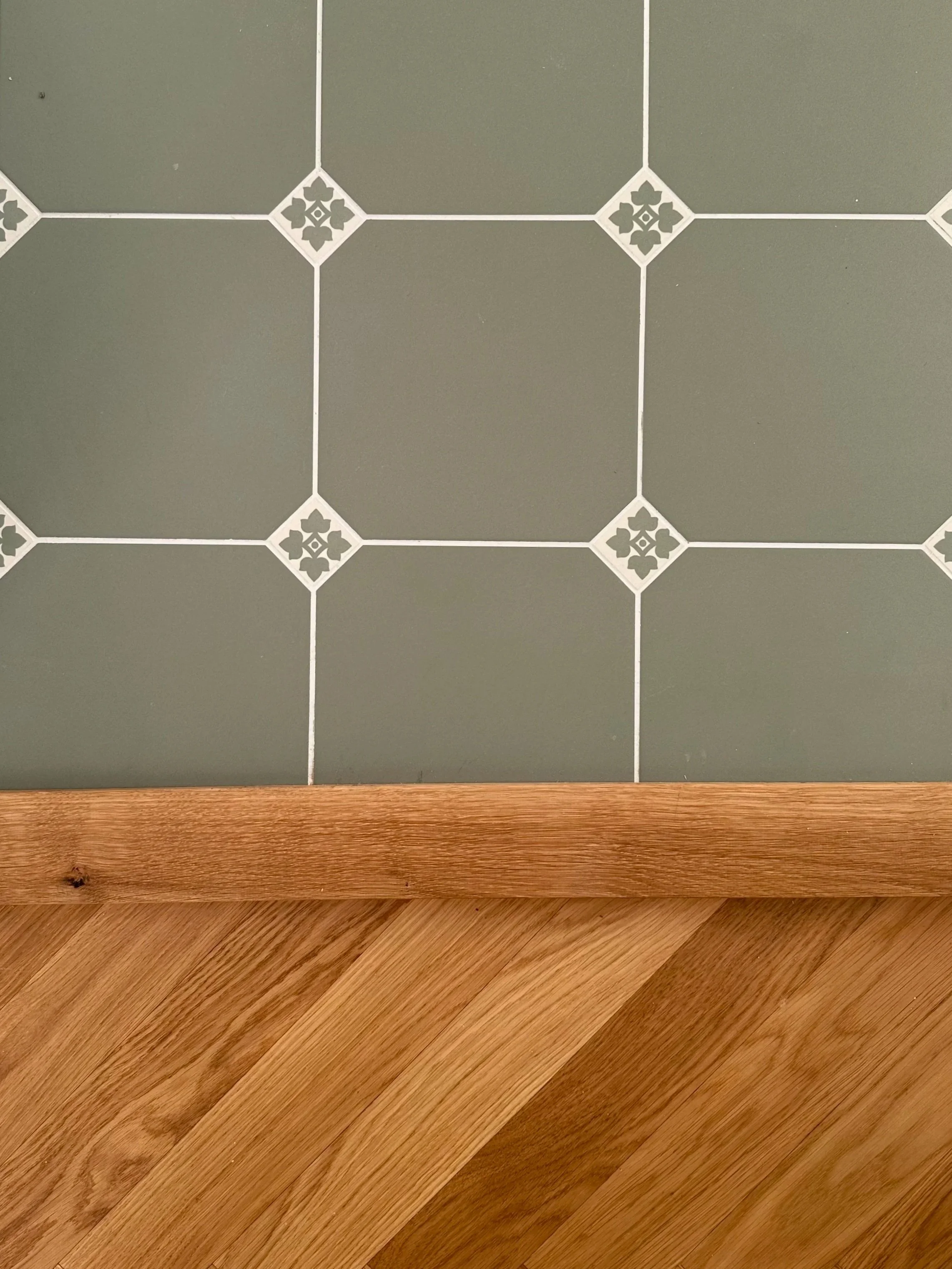 Photo of a green tiled wall with white decorative accents and a wooden floor.
