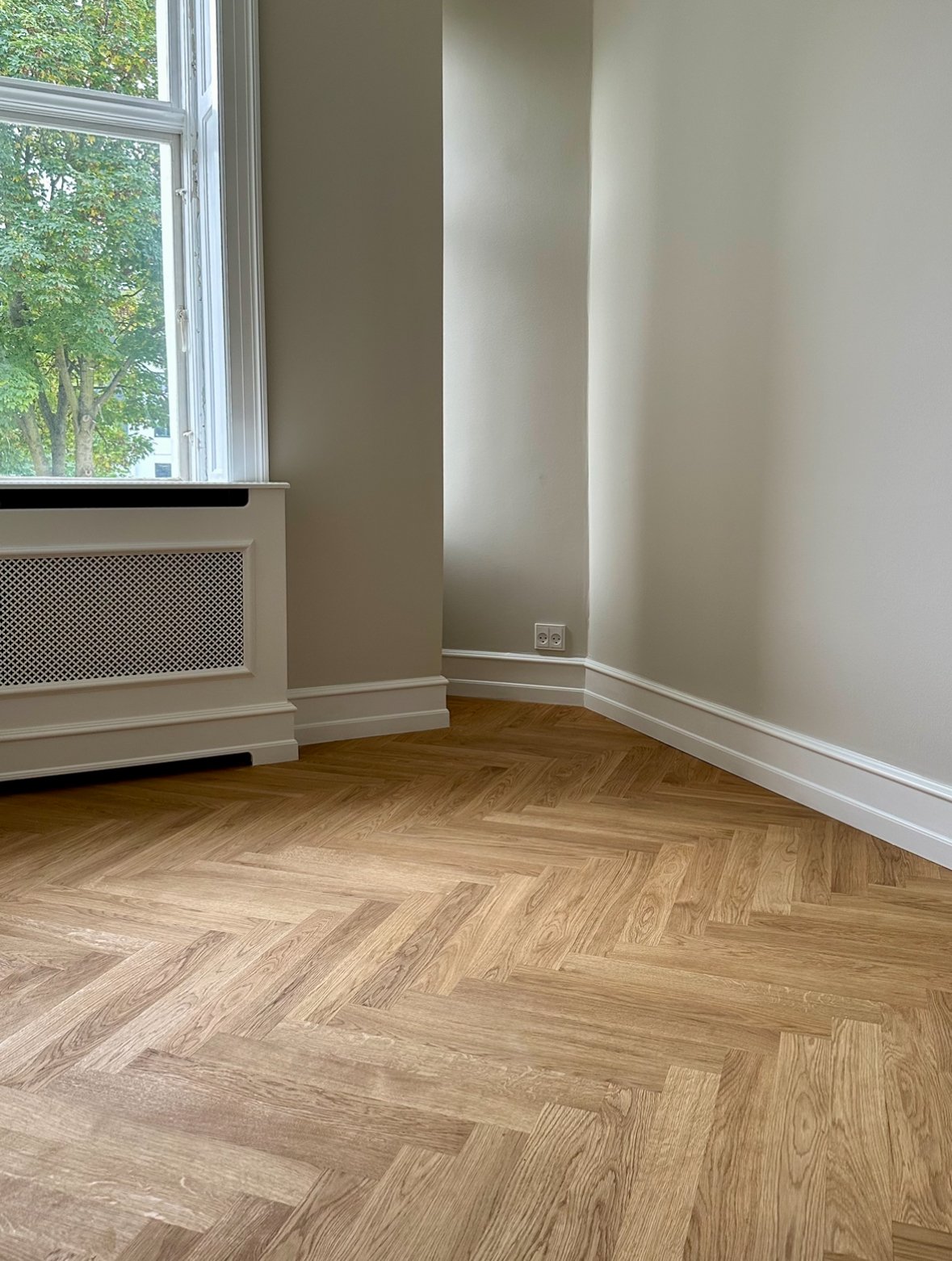 Færdigrenoveret rum med sildebensparket og specialbygget radiatorskjuler på mål.