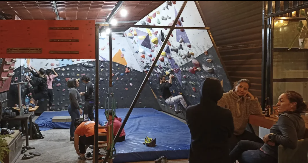 Persona practicando escalada en muro artificial dentro de un gimnasio de escalada indoor.