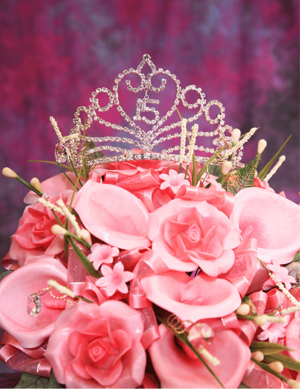 Pink bouquet with roses, flowers, green leaves, and decorative elements, topped with a sparkly tiara with the number 15.