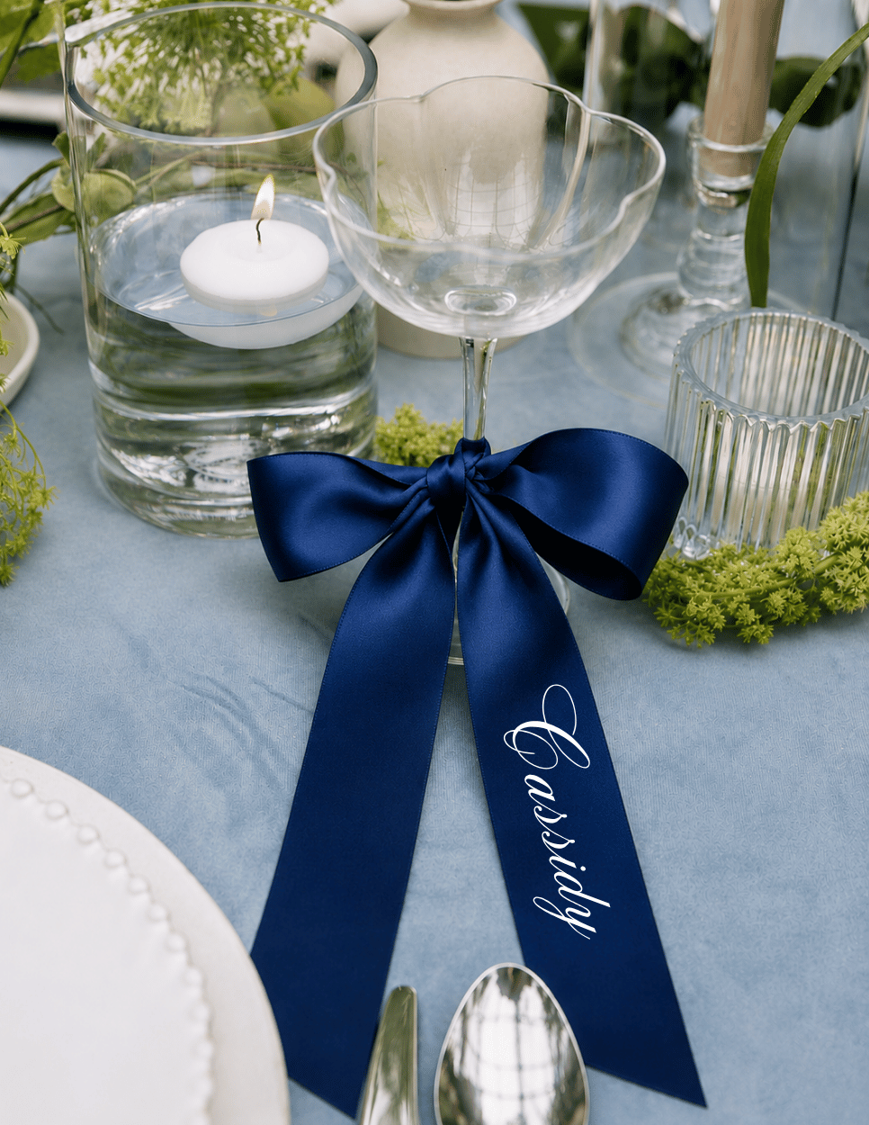 Personalized deep blue satin ribbon place card on a champagne glass for an elegant wedding reception table setting.