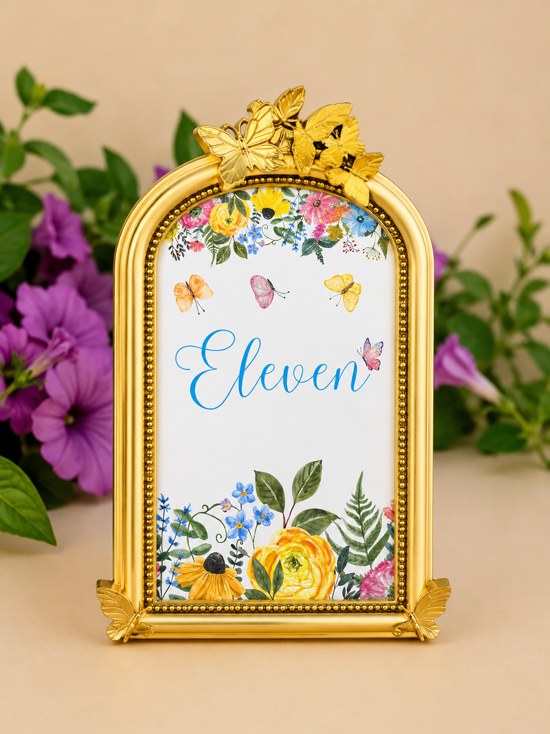 Decorative frame with butterflies and floral design, displaying the name 'Eleven' in blue script, set against a neutral background with purple flowers and green foliage.