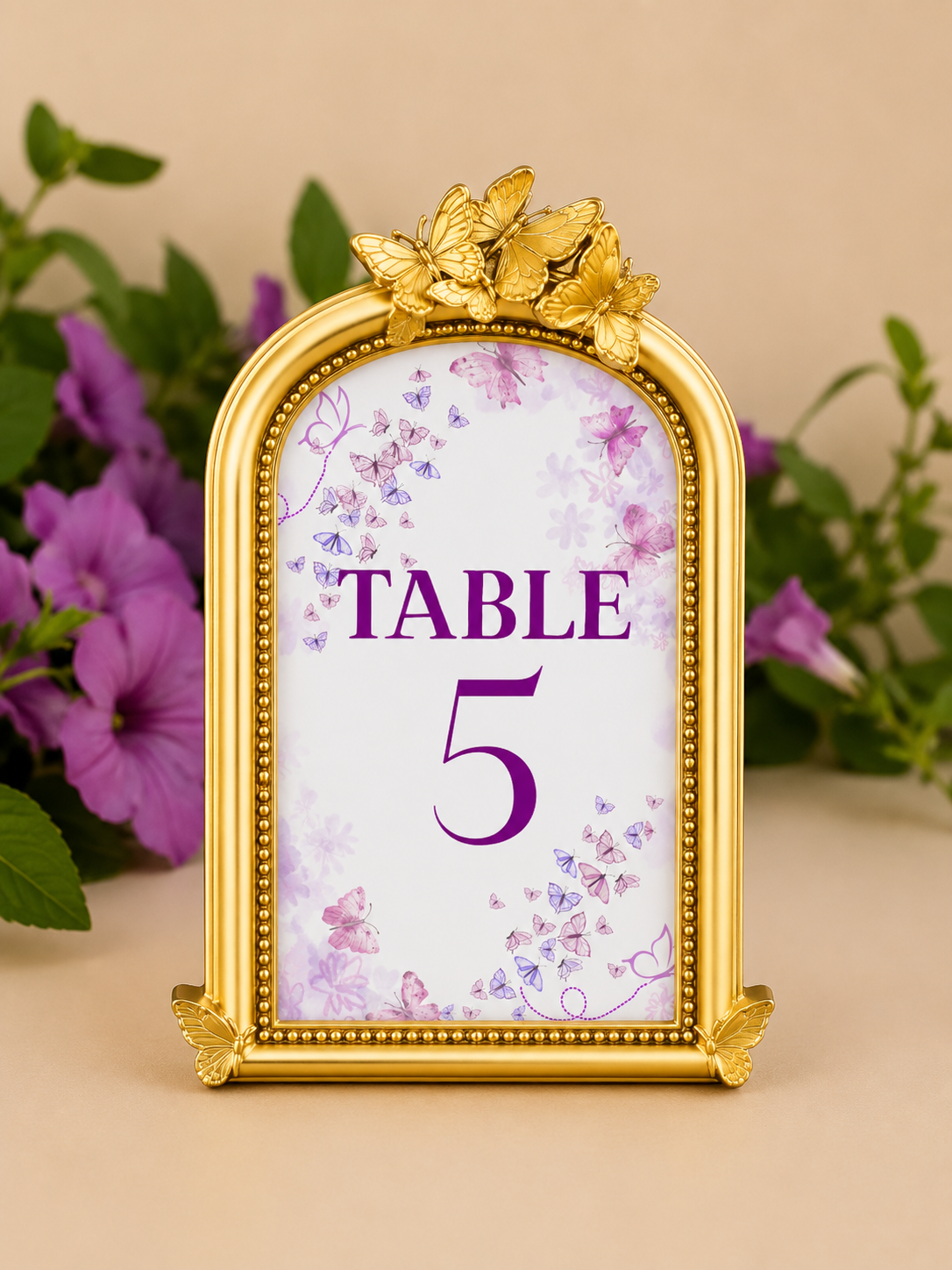 Decorative standing sign with a gold butterfly frame, floral and butterfly patterns, indicating table 5, with purple and pink butterfly motifs and purple lettering, set against purple flowers and green leaves.