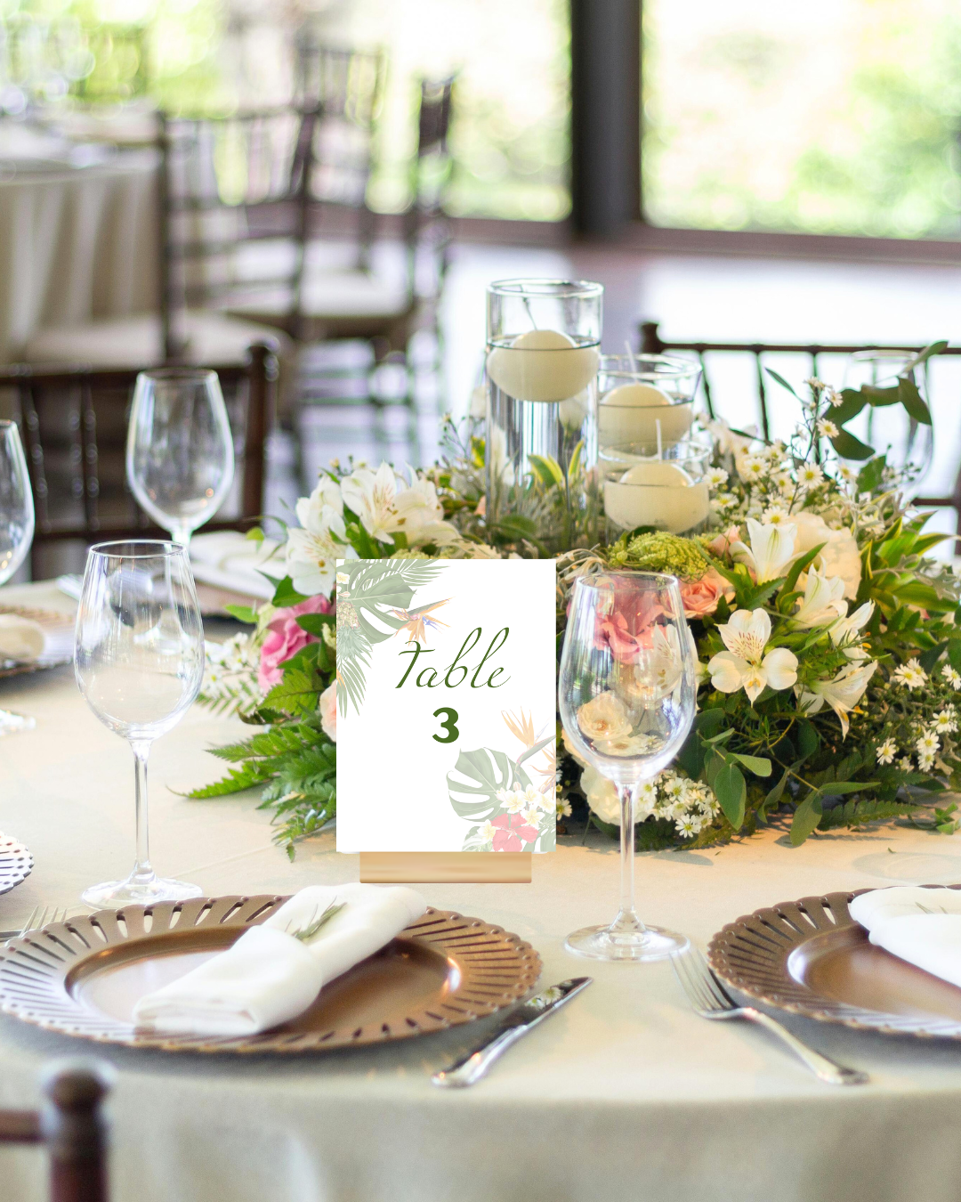 A banquet table set for a wedding or event with floral arrangements, glassware, and place settings. There is a tropical tabler number card indicating "Table 3."